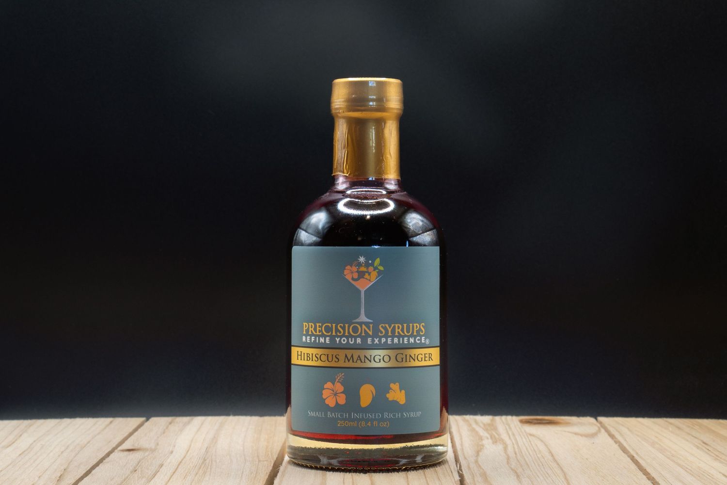 Dark spirits bottle with gold cap and tree emblem photographed against black background.