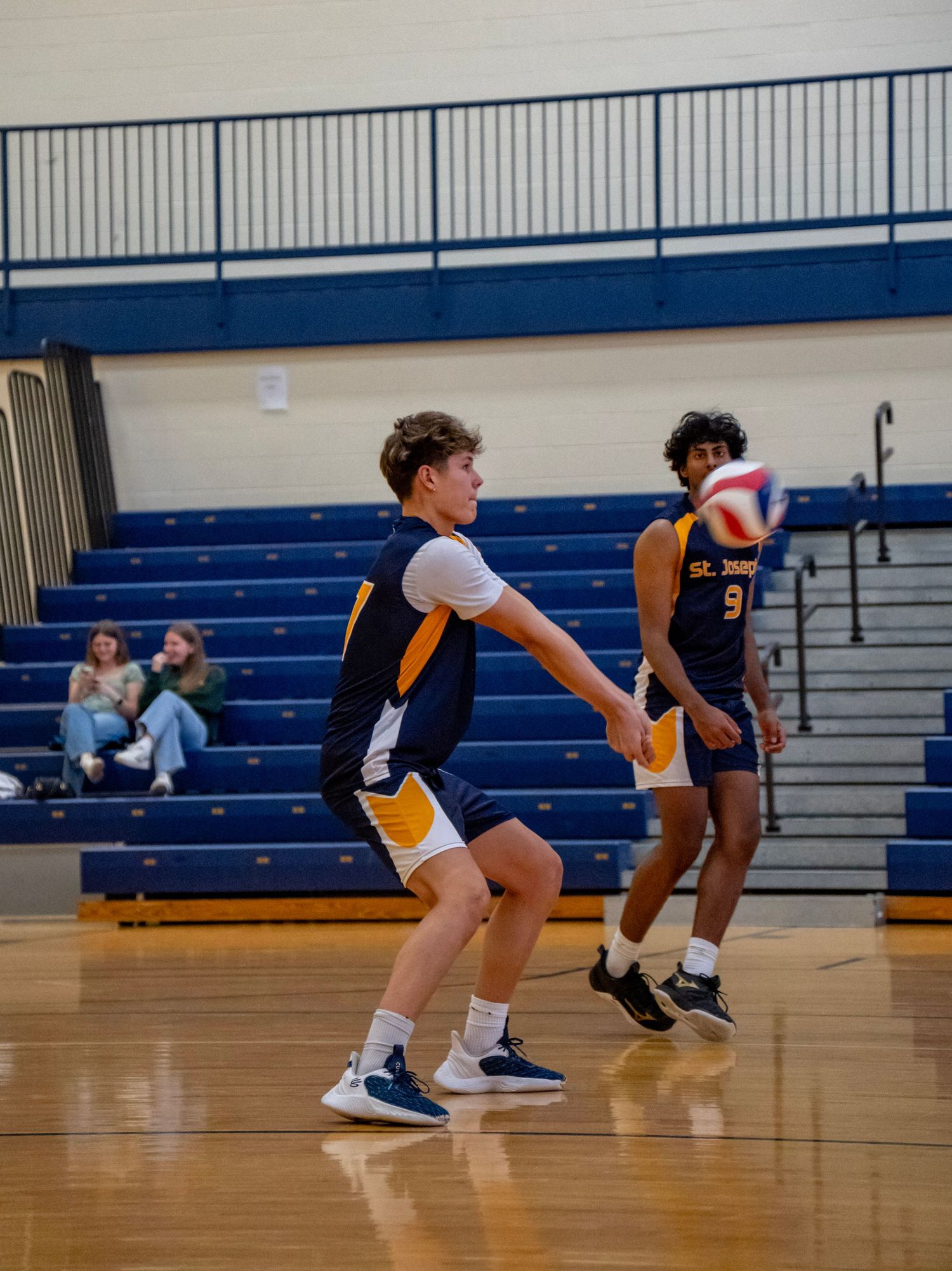 Two players in navy and gold uniforms prepare for play on volleyball court.