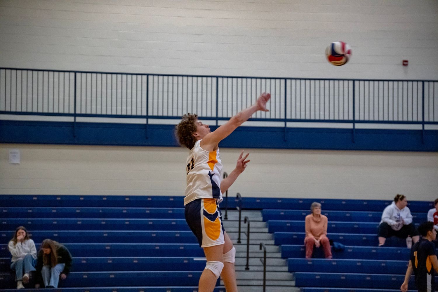 Player reaches up to block volleyball during competitive indoor game with spectators watching.