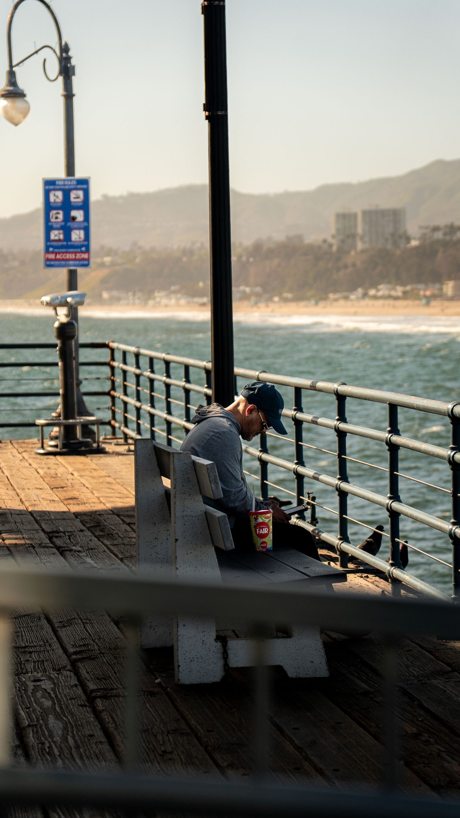 Person sitting on wooden pier with vintage lampposts and ocean view.