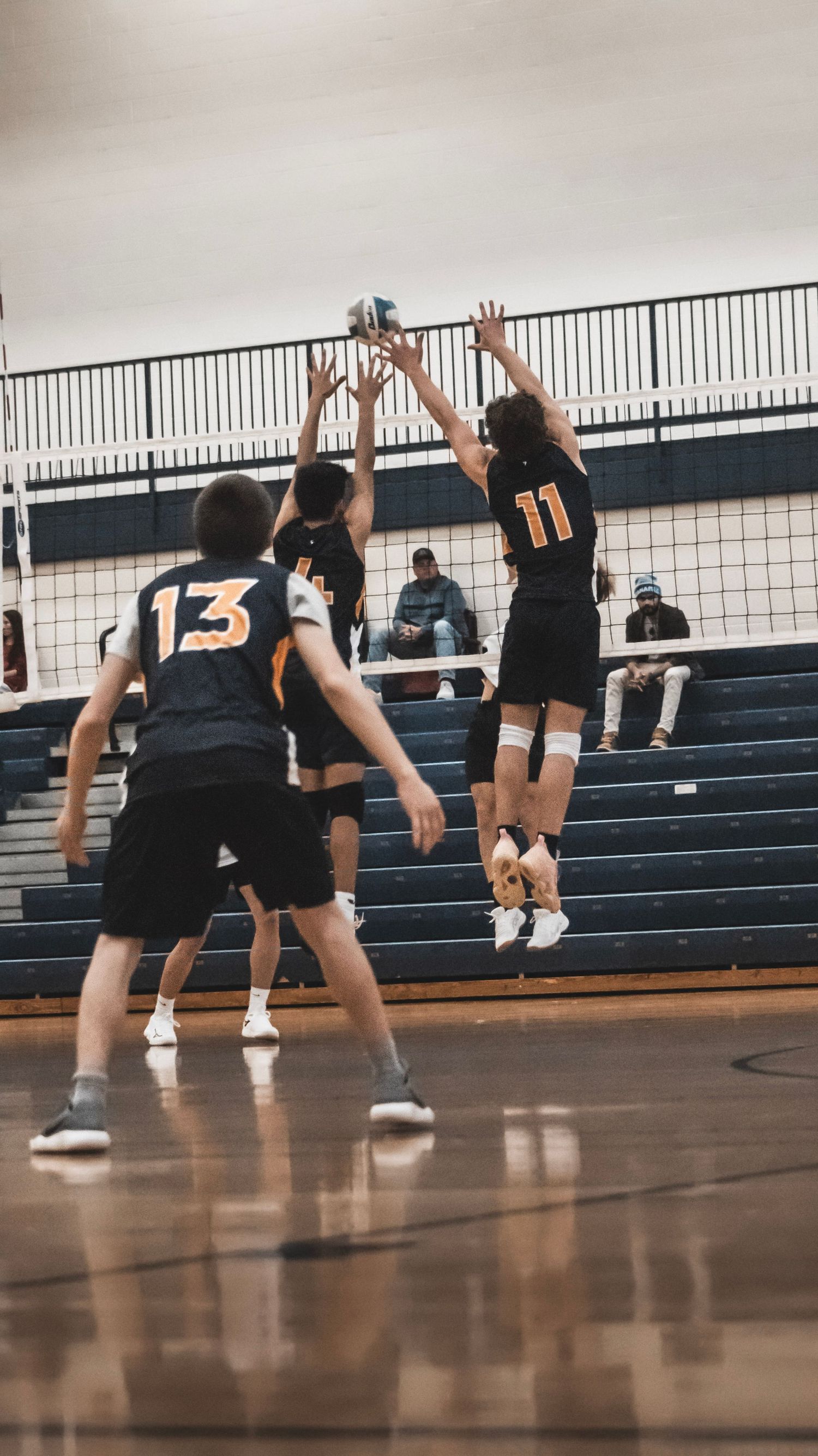 Volleyball players leap at net for block during intense indoor game action.