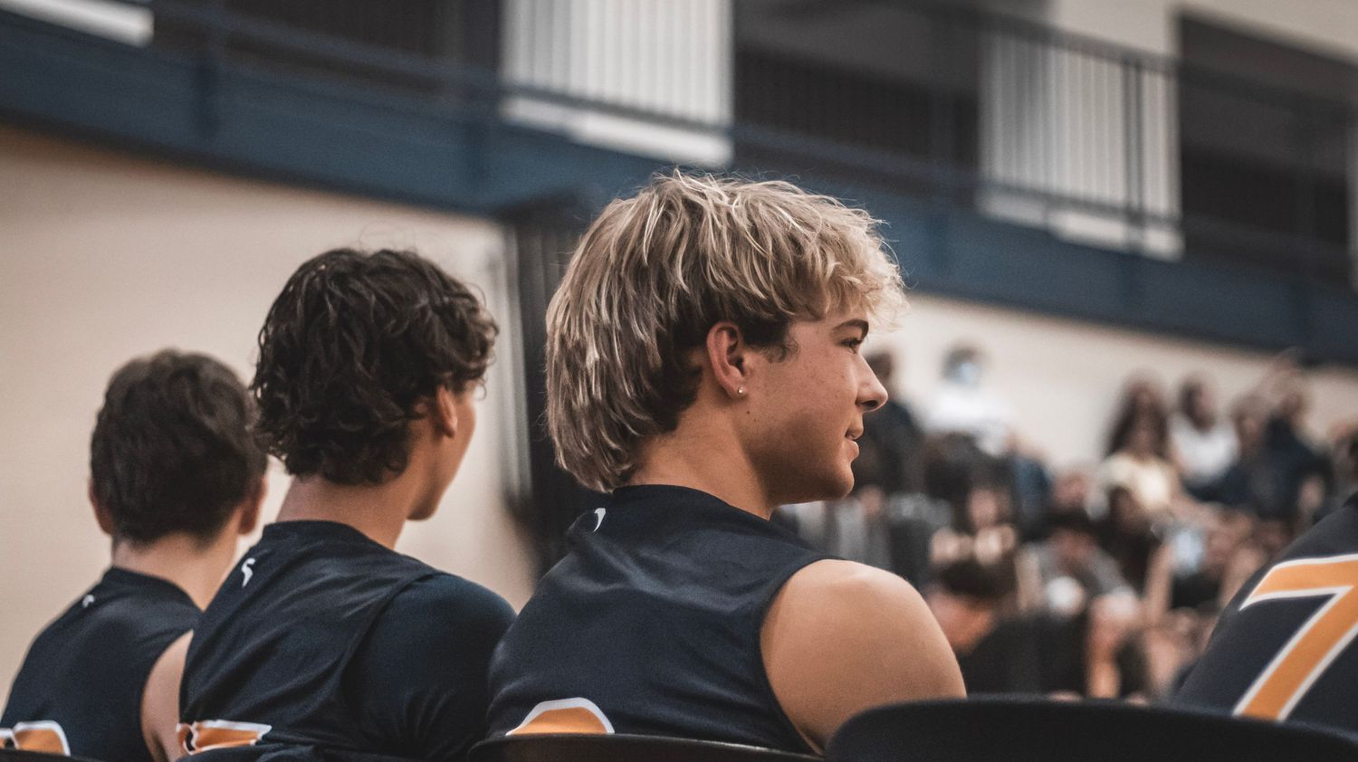 Players watch from the sidelines during a high school volleyball match.