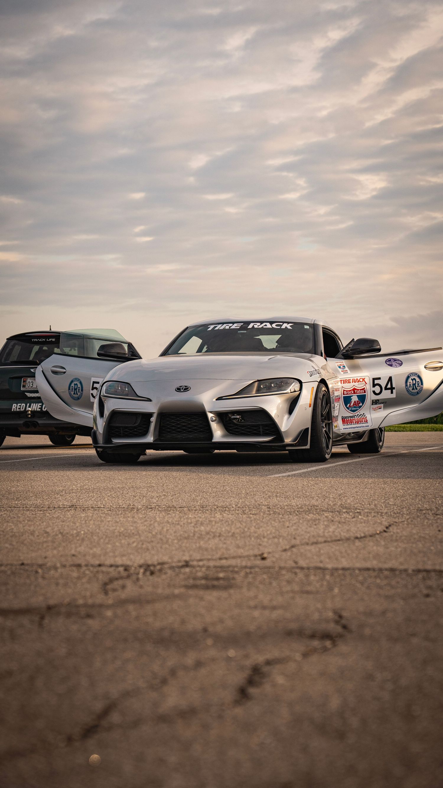 White Toyota Supra race car with number 54 decal positioned among other vehicles.
