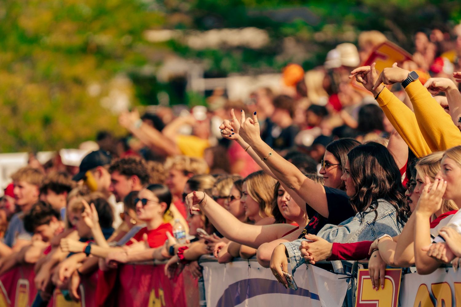 Crowd of festival attendees raise their hands in unison during an outdoor music performance.