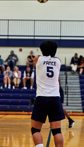 Volleyball player wearing white jersey number 5 standing on indoor court during game.