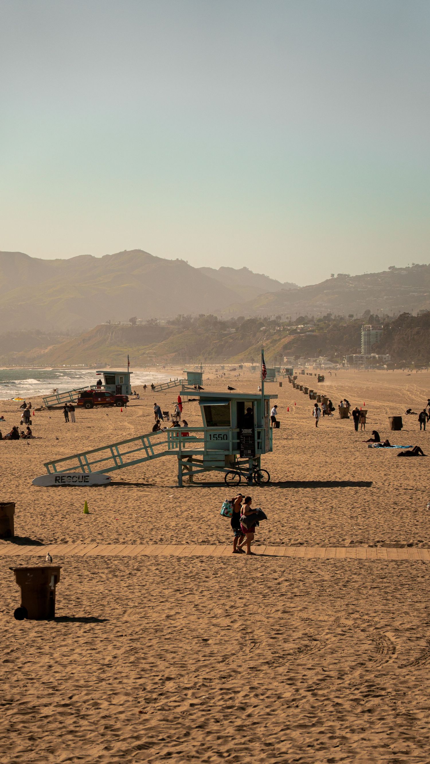 Sunny beach scene with lifeguard towers and people enjoying the California coastline.