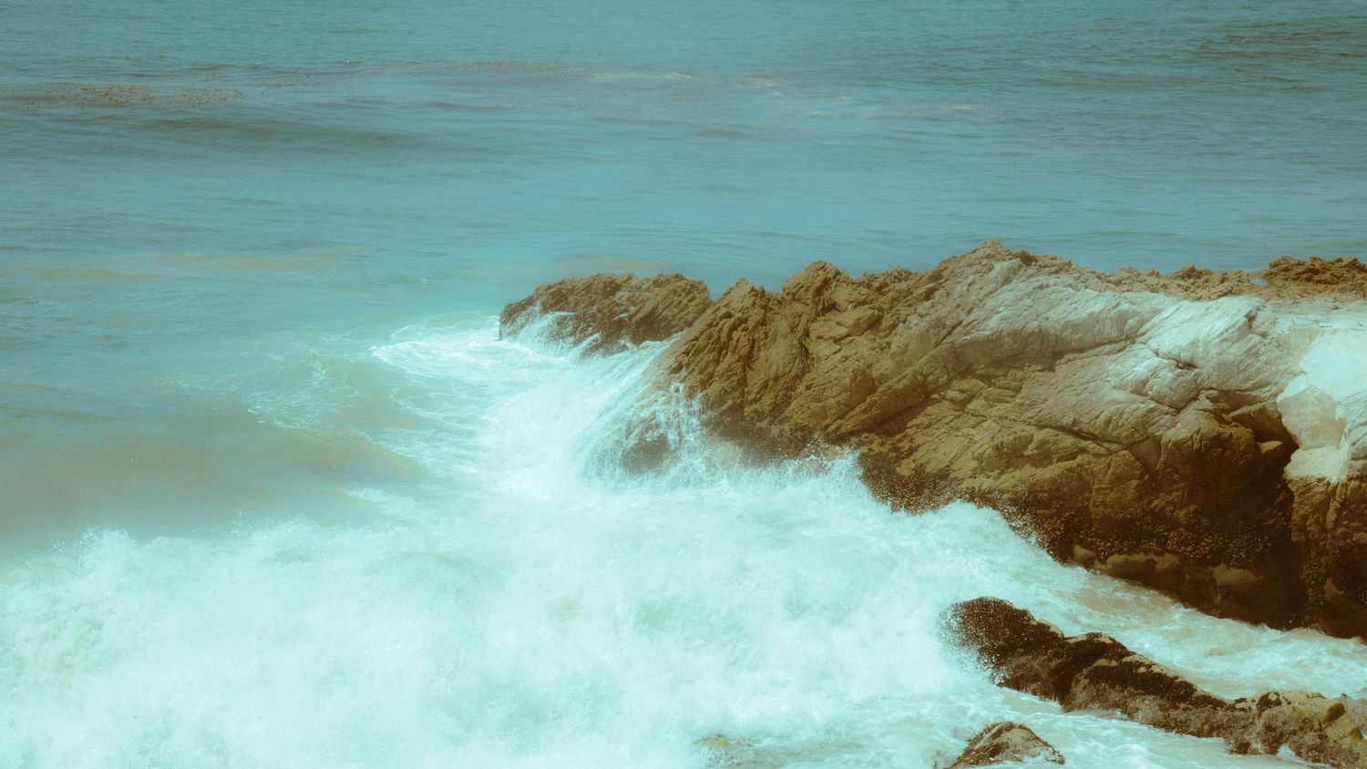 Dramatic ocean waves crashing against rocky coastal cliffs in turquoise waters.