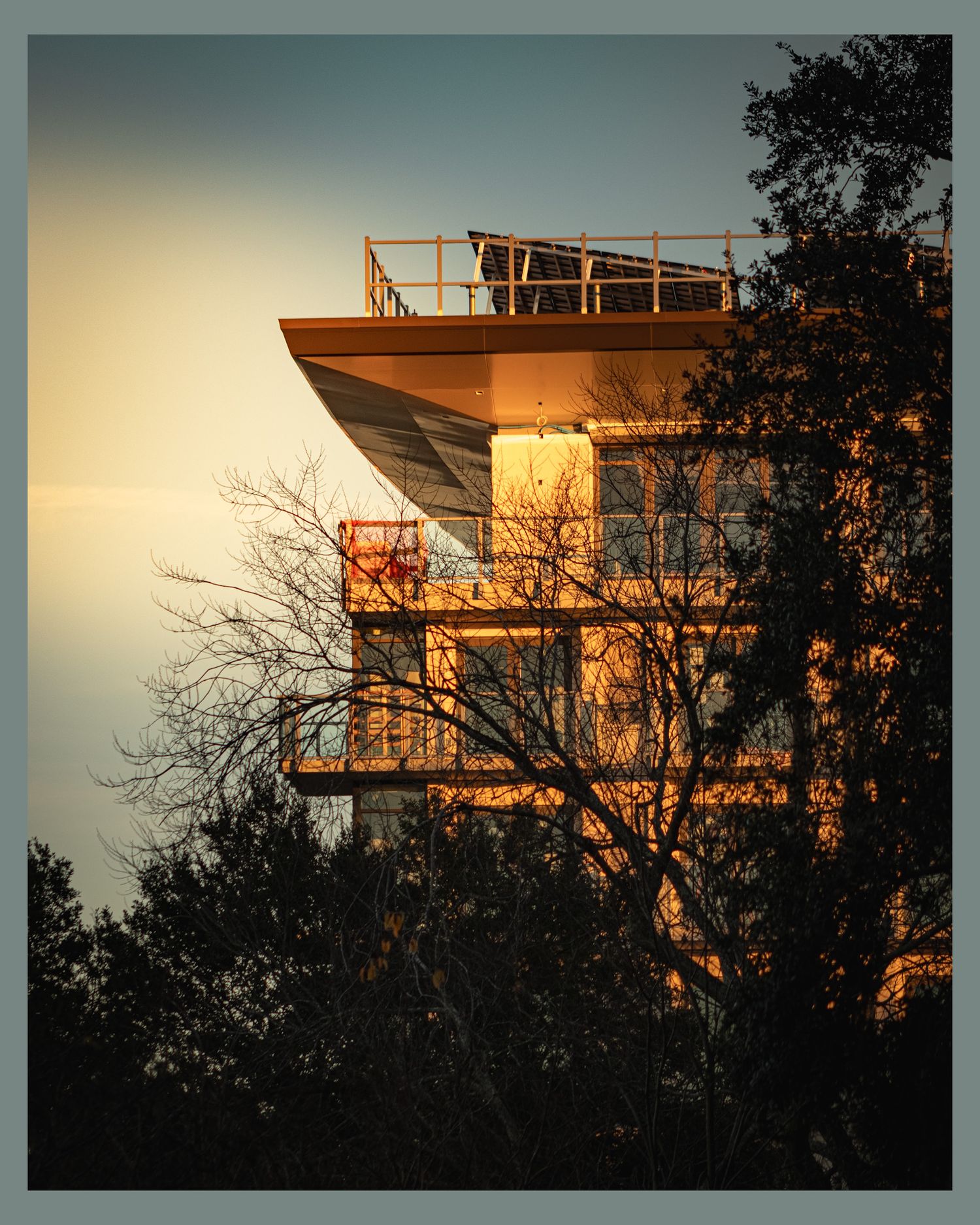 Modern observation tower glowing in golden sunset light among silhouetted trees.