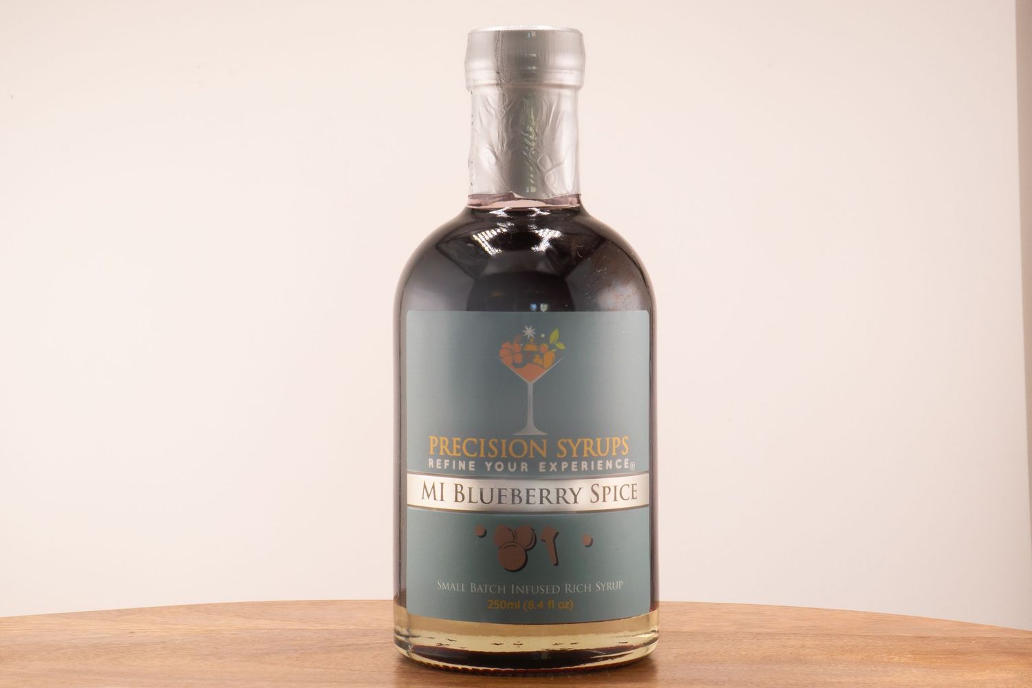 A bottle of specialty cranberry sauce syrup with elegant gray and red label on wooden surface.