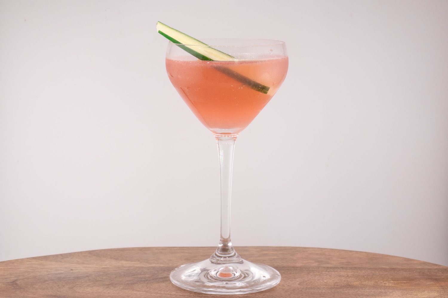 Pink martini cocktail garnished with a lemongrass stalk in a stemmed glass.