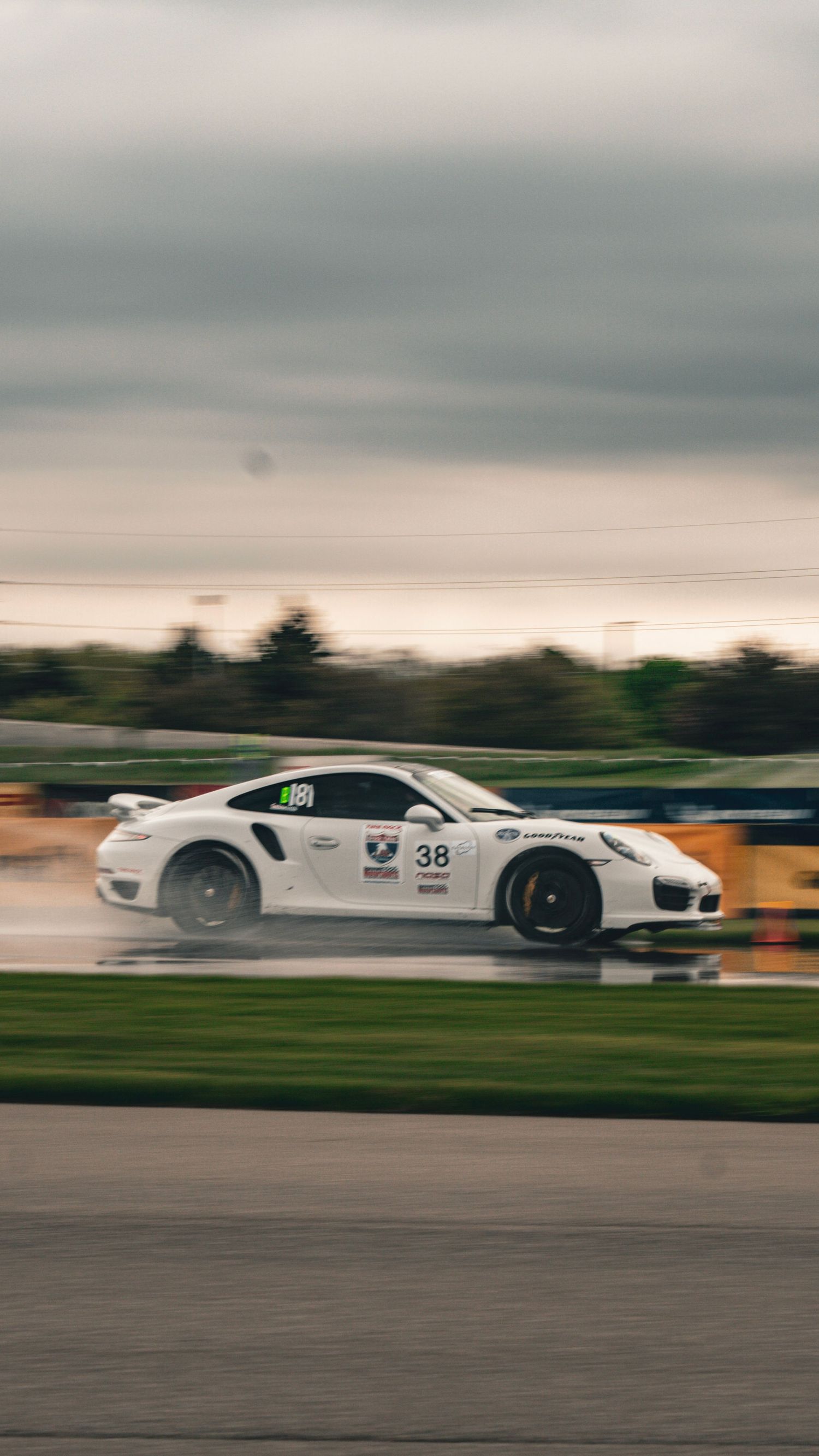 White Porsche race car drifting on wet racing circuit.