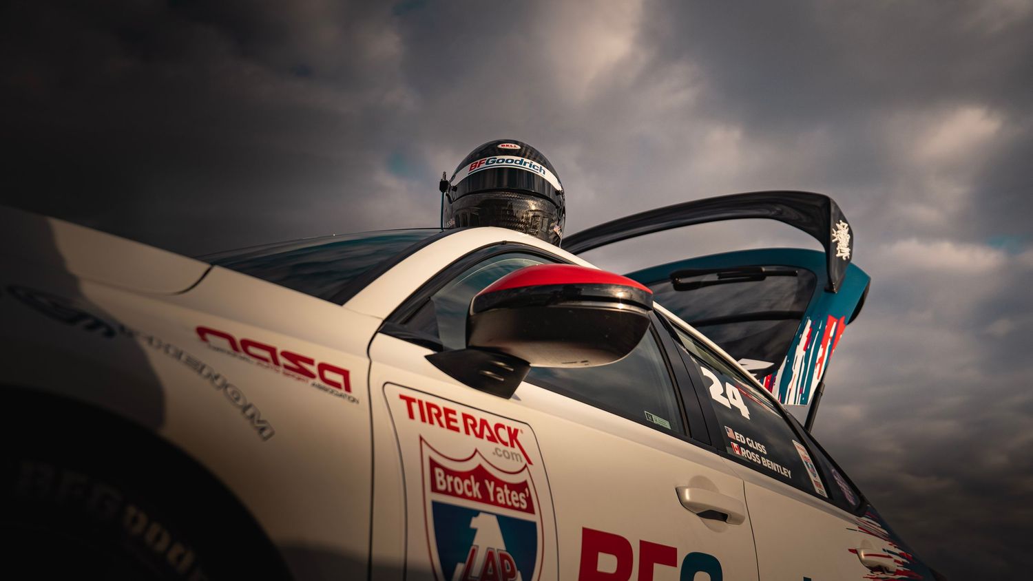 Low angle shot of white race car with Tire Rack branding under dramatic cloudy sky.