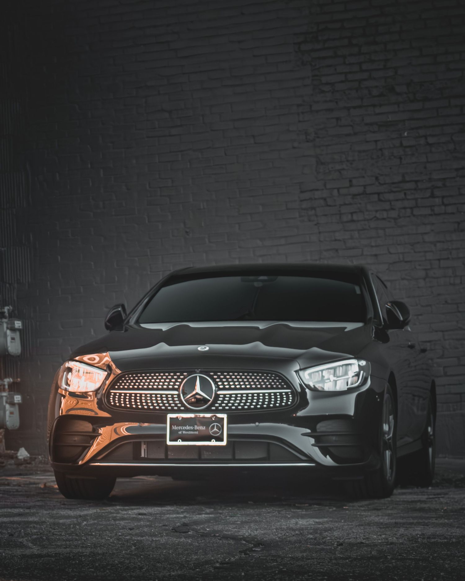 Mercedes-Benz sedan with illuminated grille photographed at night against brick wall.