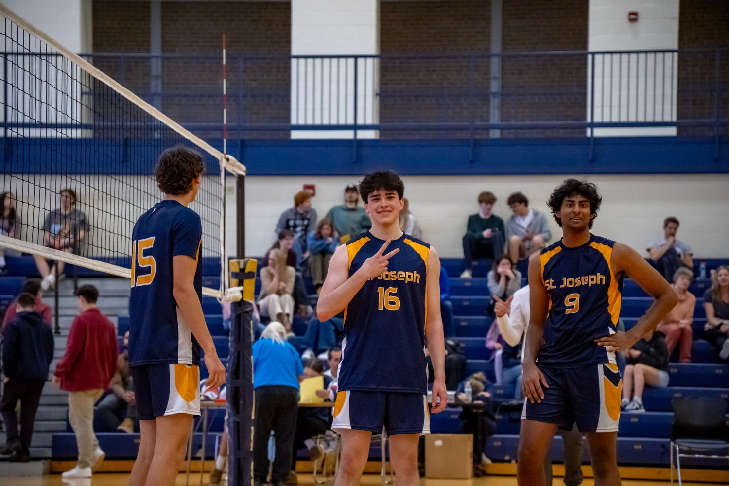 High school volleyball players in navy blue uniforms stand together during a match in a gymnasium.