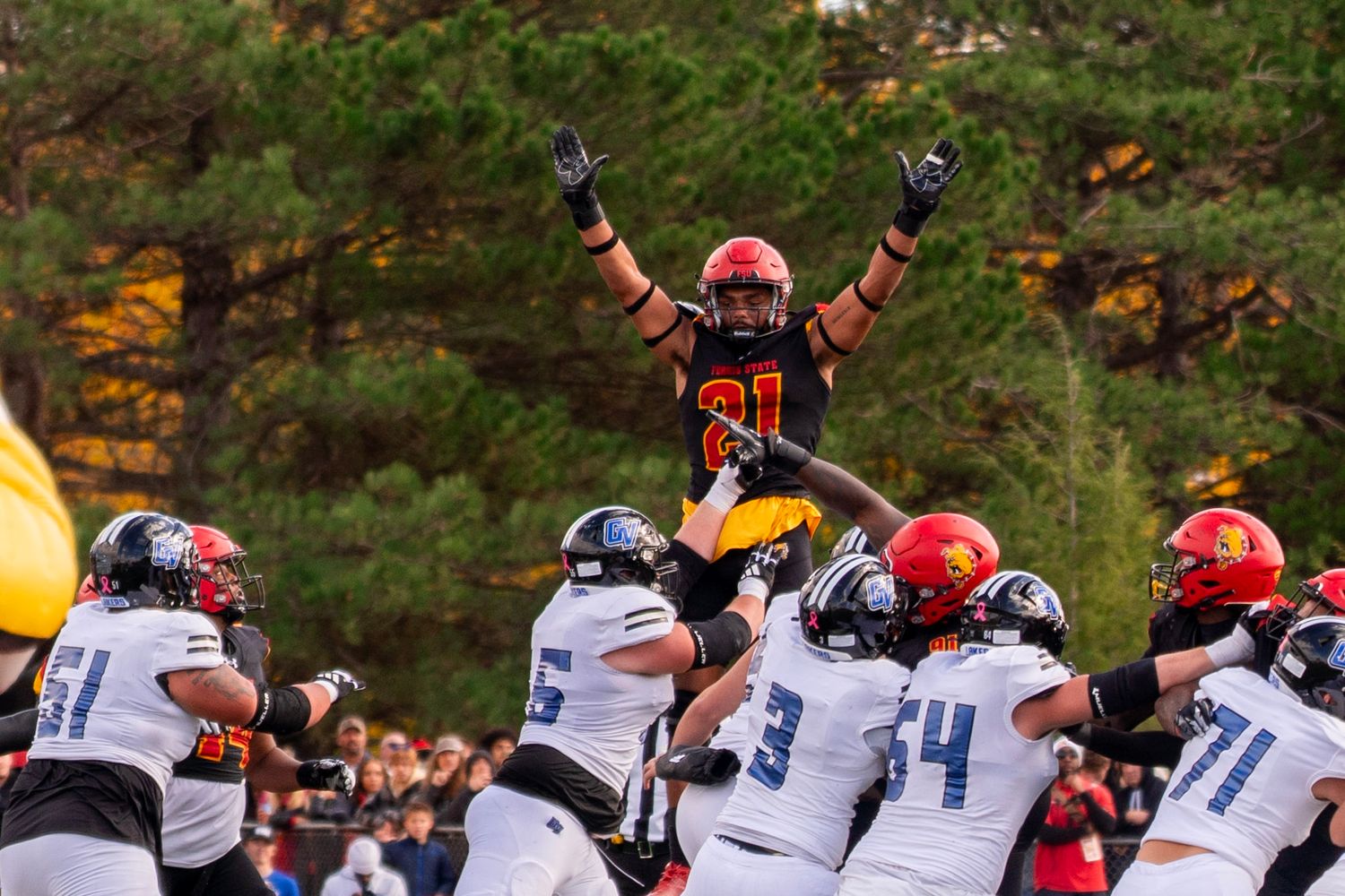Football player celebrates victory by being lifted up by teammates during an exciting game moment.