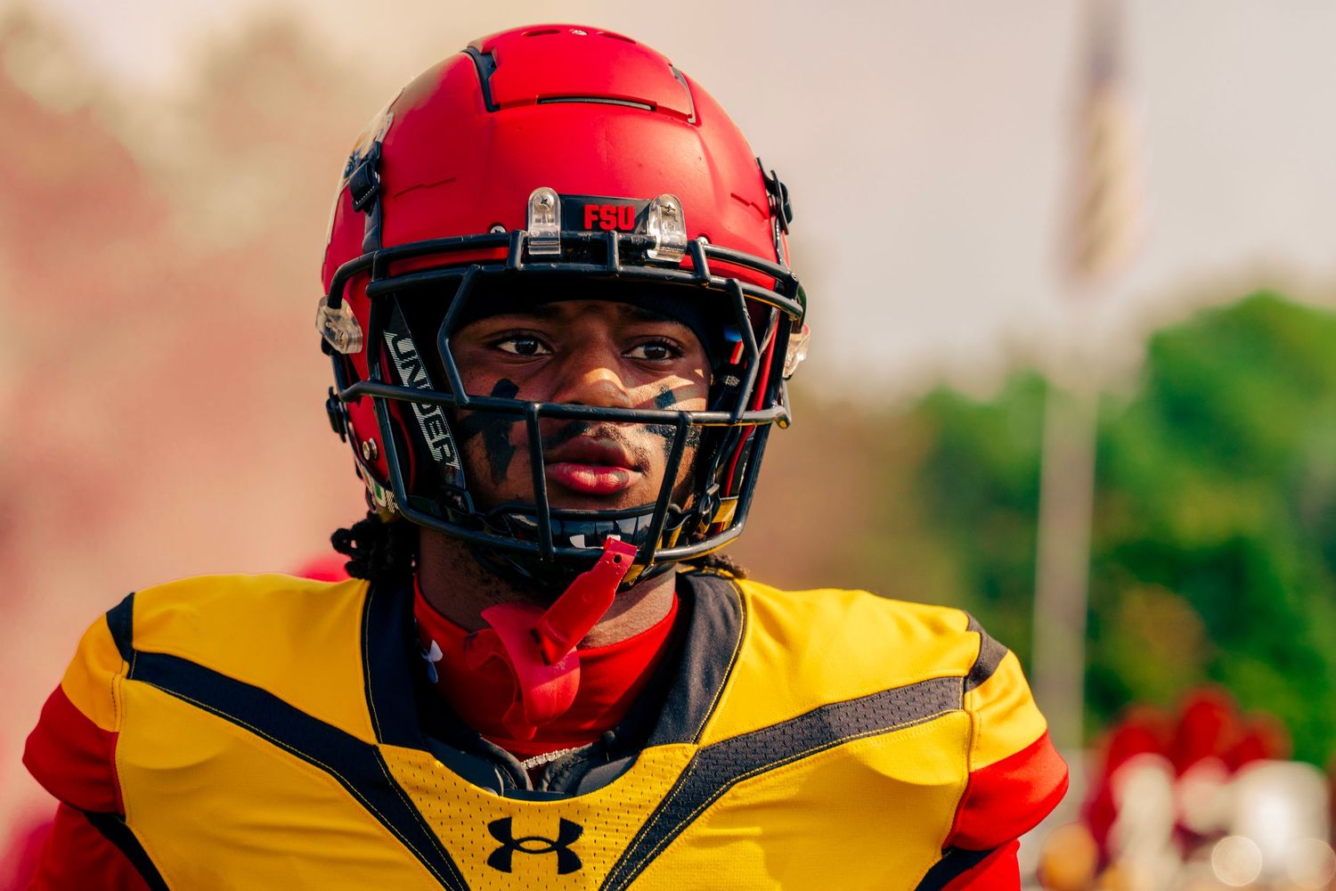 Football players in red helmets and yellow jerseys line up on the field during a game.