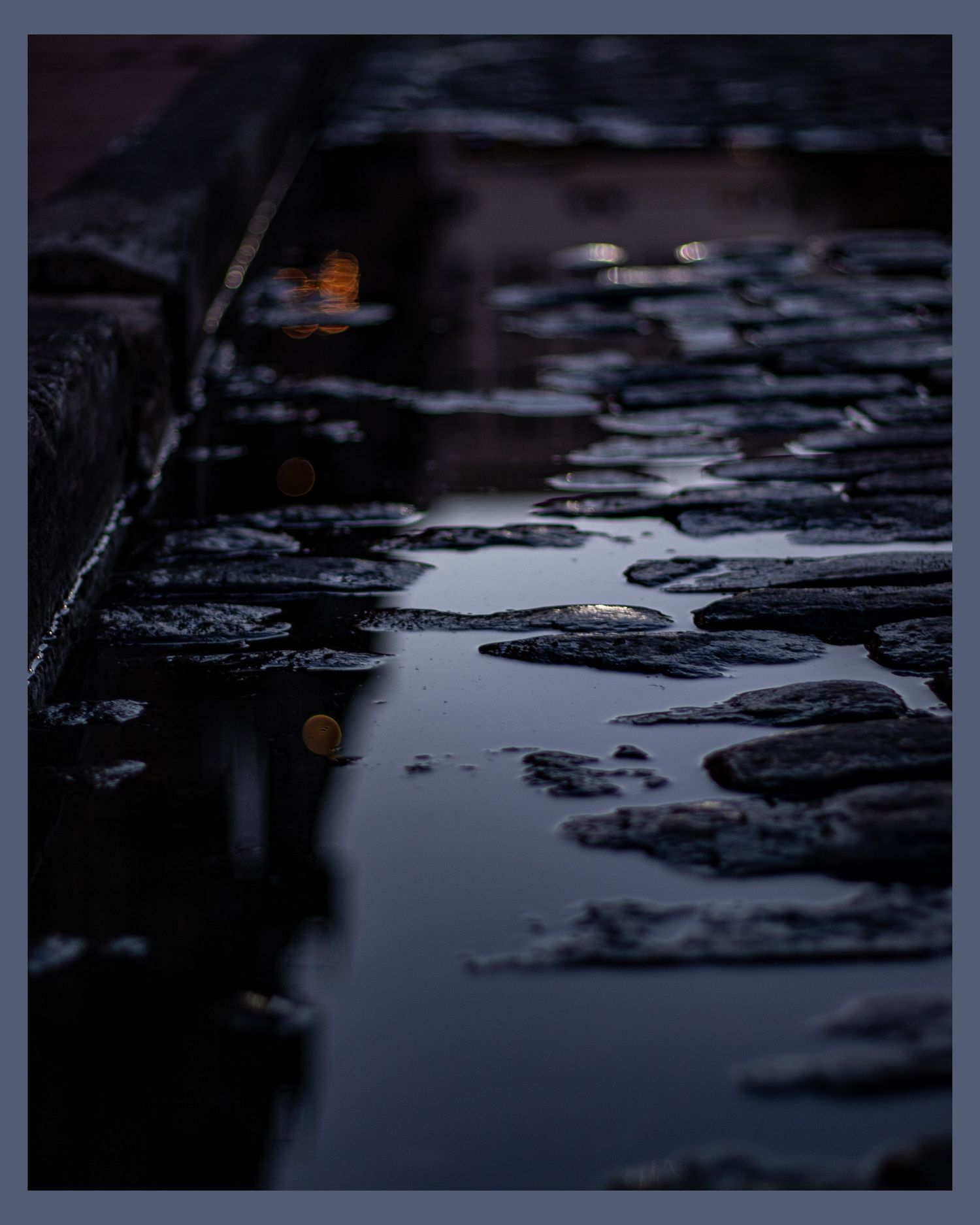 Wet cobblestone street reflecting lights at night in moody atmosphere.
