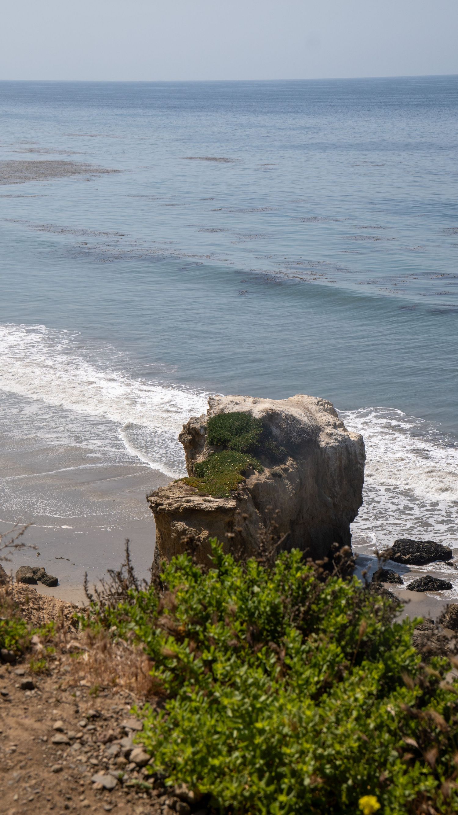 Large solitary rock formation stands amid crashing waves on a scenic beach.