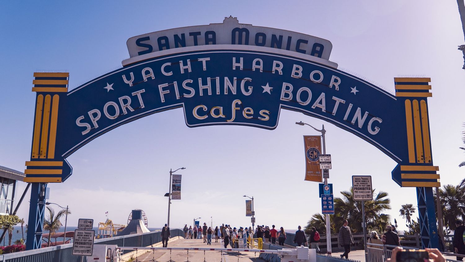 Santa Monica Yacht Harbor entrance arch with pedestrians walking beneath on sunny day.
