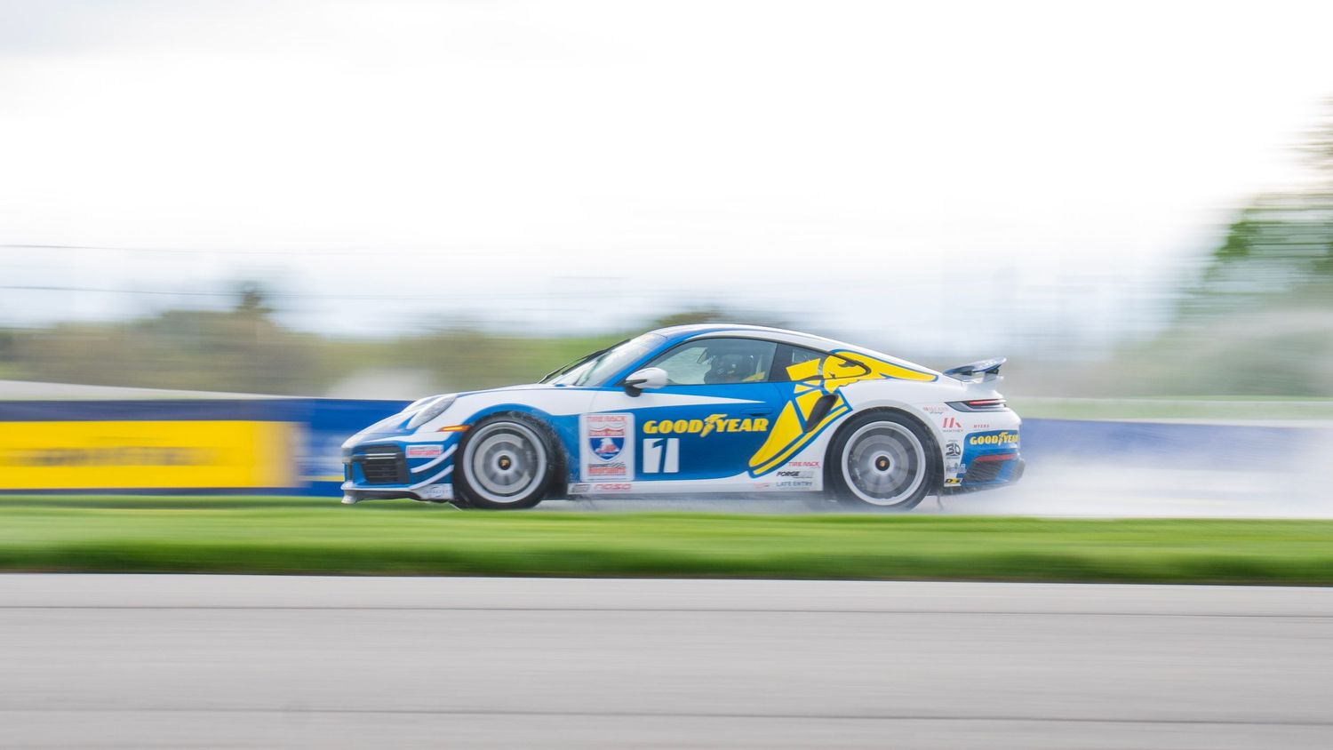 Porsche GT3 race car speeding along a racetrack with blue and yellow motion blur in the background.