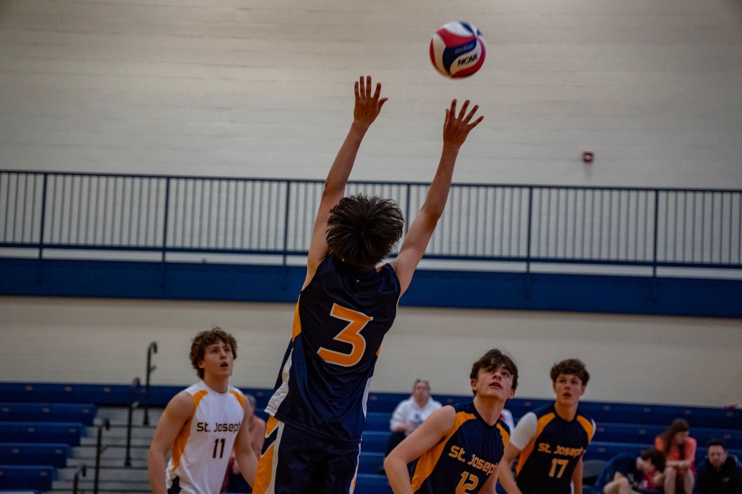 Player in navy jersey jumps to block volleyball during competitive match.