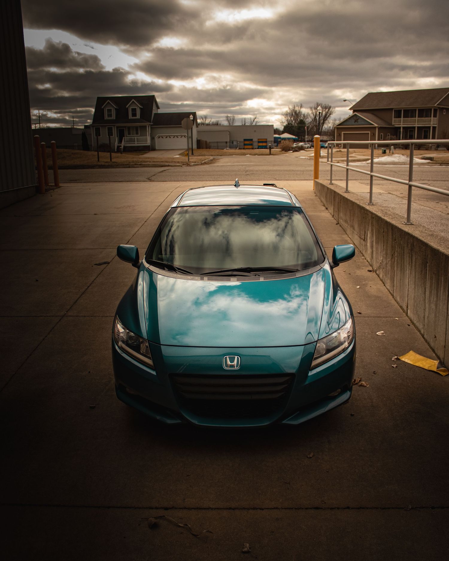 Teal Honda CR-Z photographed from above in empty parking lot under moody sky.