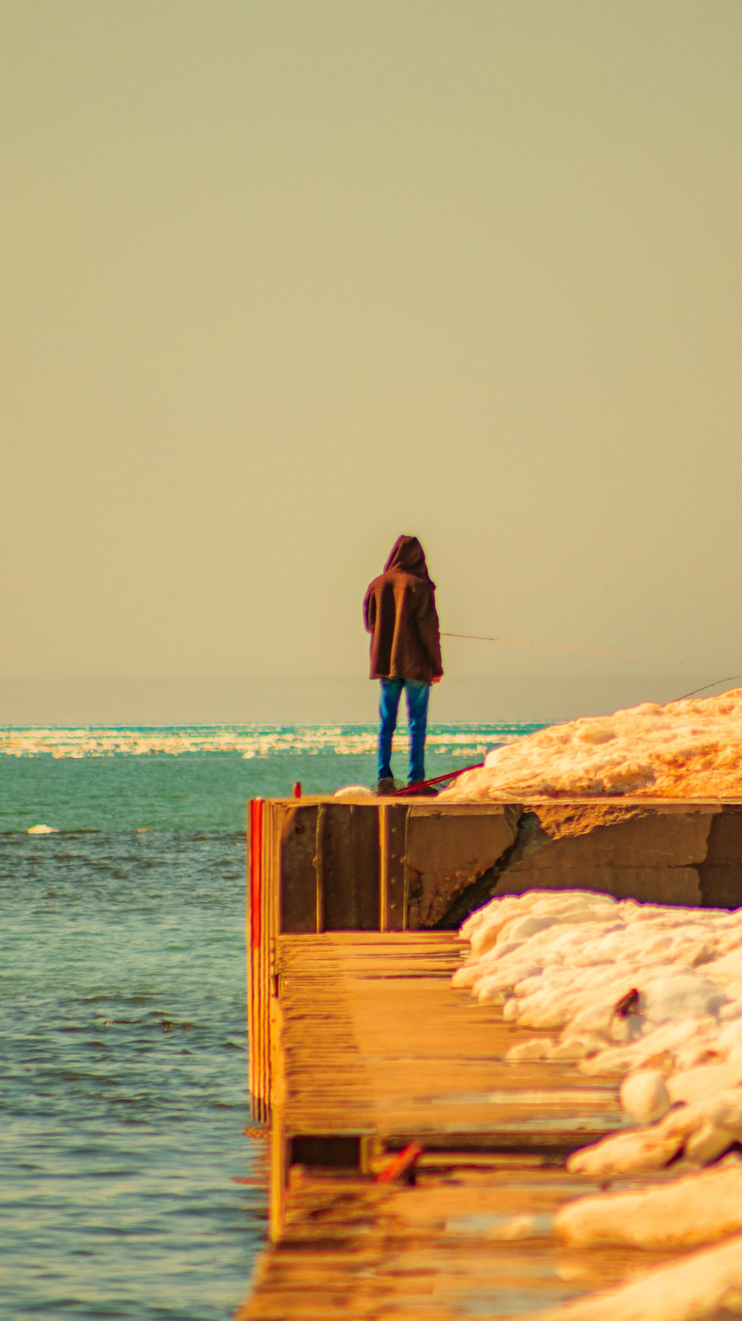 Person in red coat standing on snowy pier overlooking winter waters.