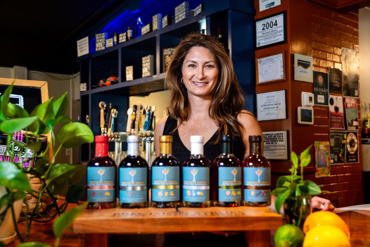 Display of blue-labeled bottles on wooden shelf with decorative plants and warm interior lighting.