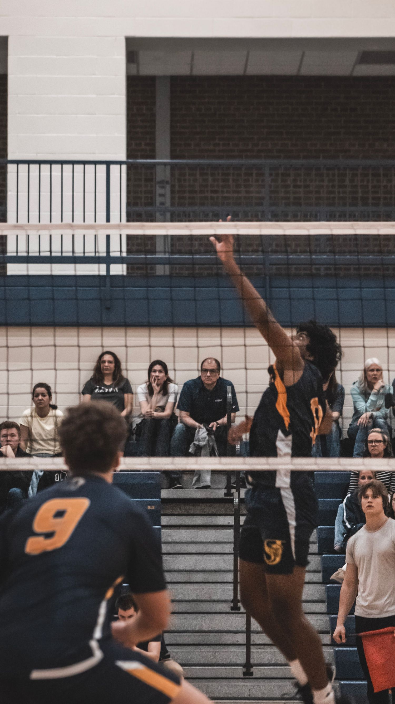 Player reaches up to block shot at net during competitive indoor volleyball game.