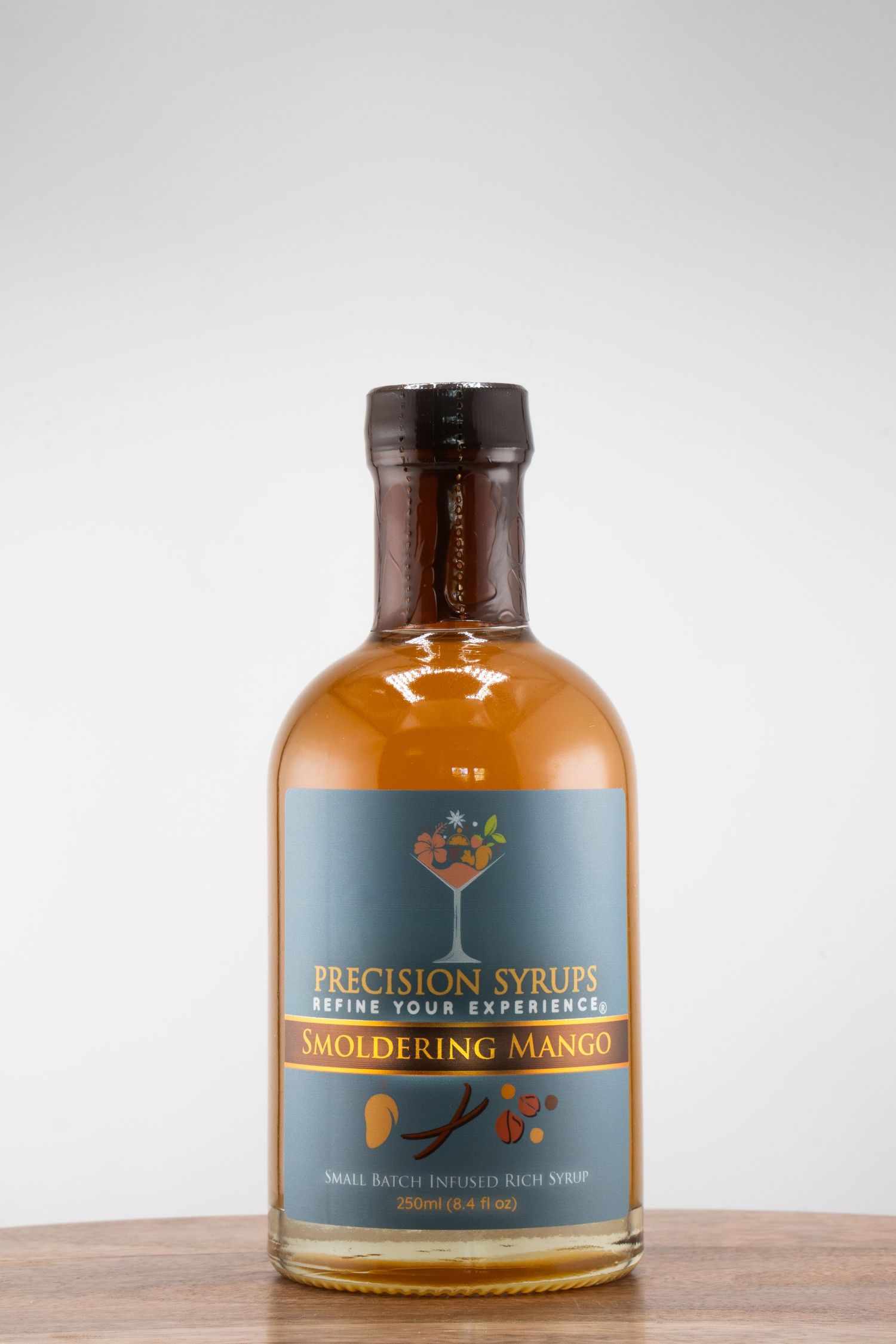 A bottle of Smoked King Mango Precision Syrup with amber liquid against a light background.