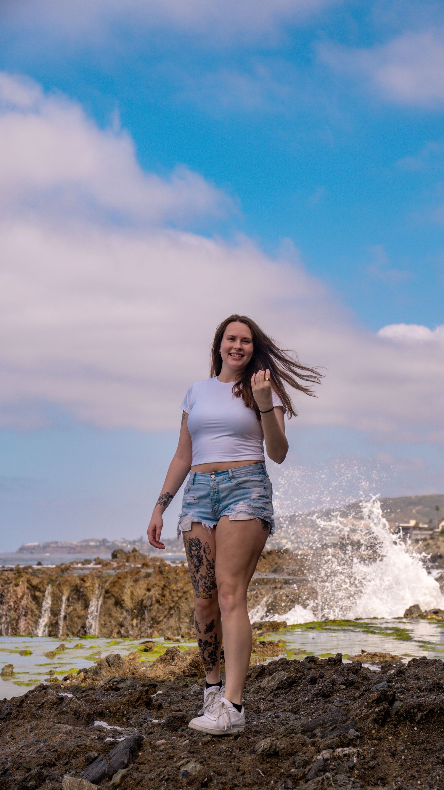 Someone standing on volcanic rocks as ocean waves crash against the shore.