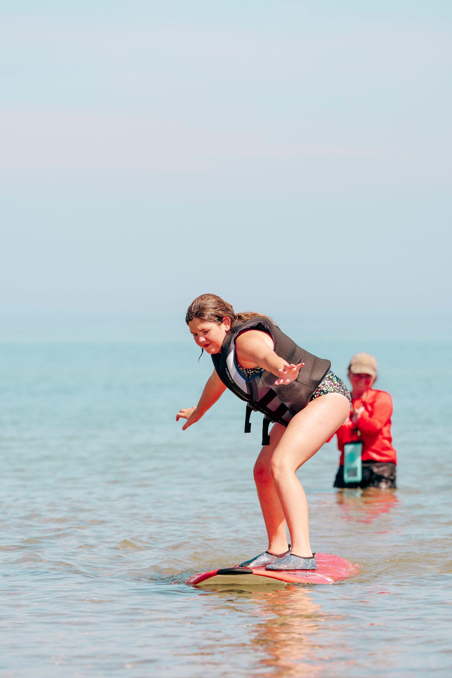 A surfer demonstrates skimboarding moves in shallow coastal waters on a bright sunny day.