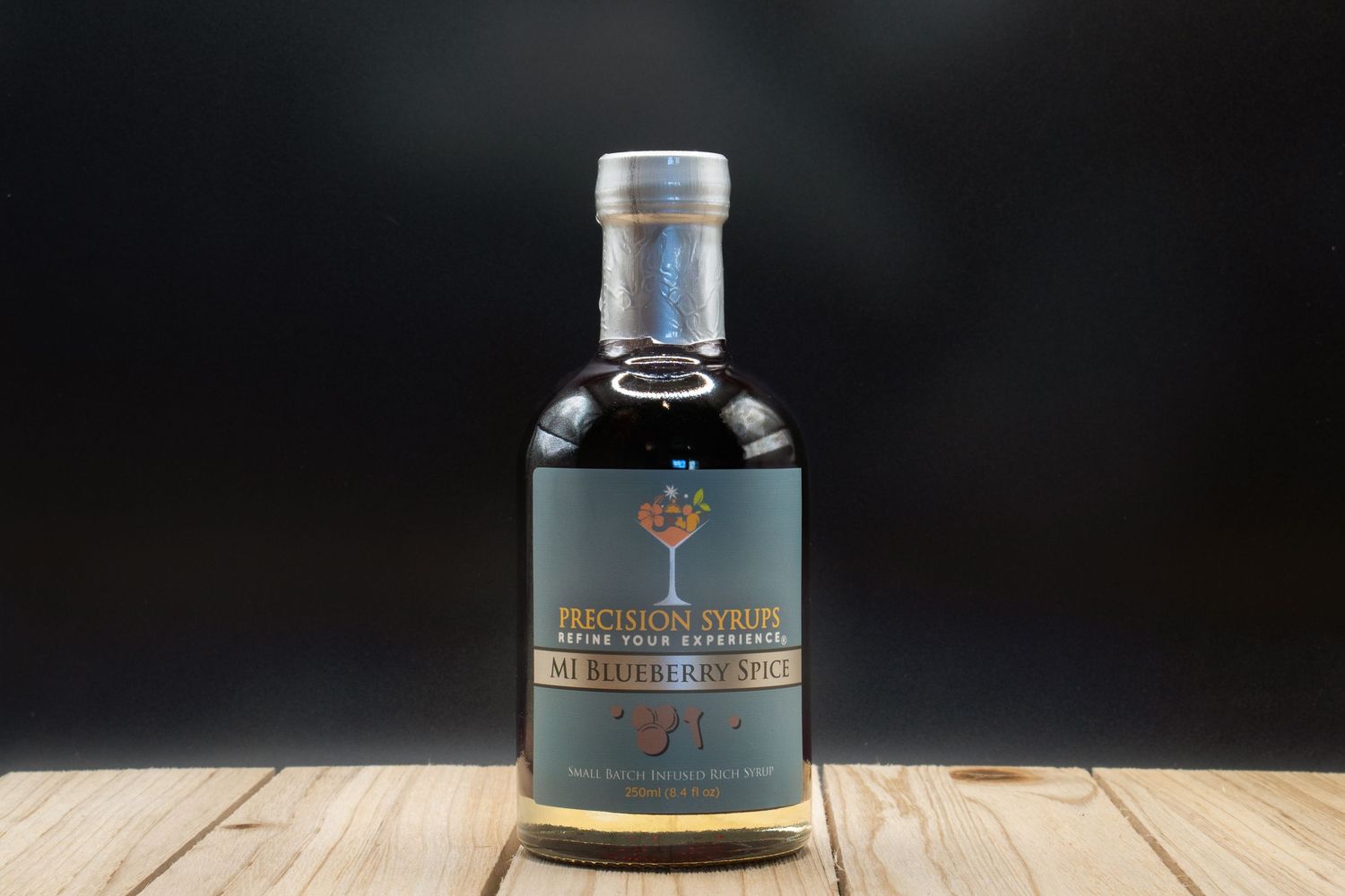 A bottle of Precision Syrups craft cocktail mixer with dark liquid against a black background.