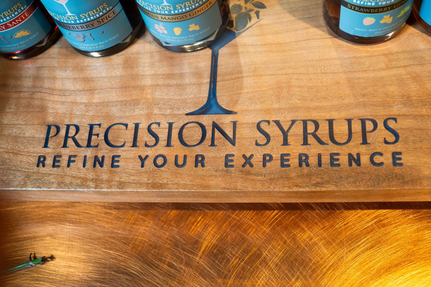 Wooden surface with 'Precision Syrups' logo text and blue bottles in the background.