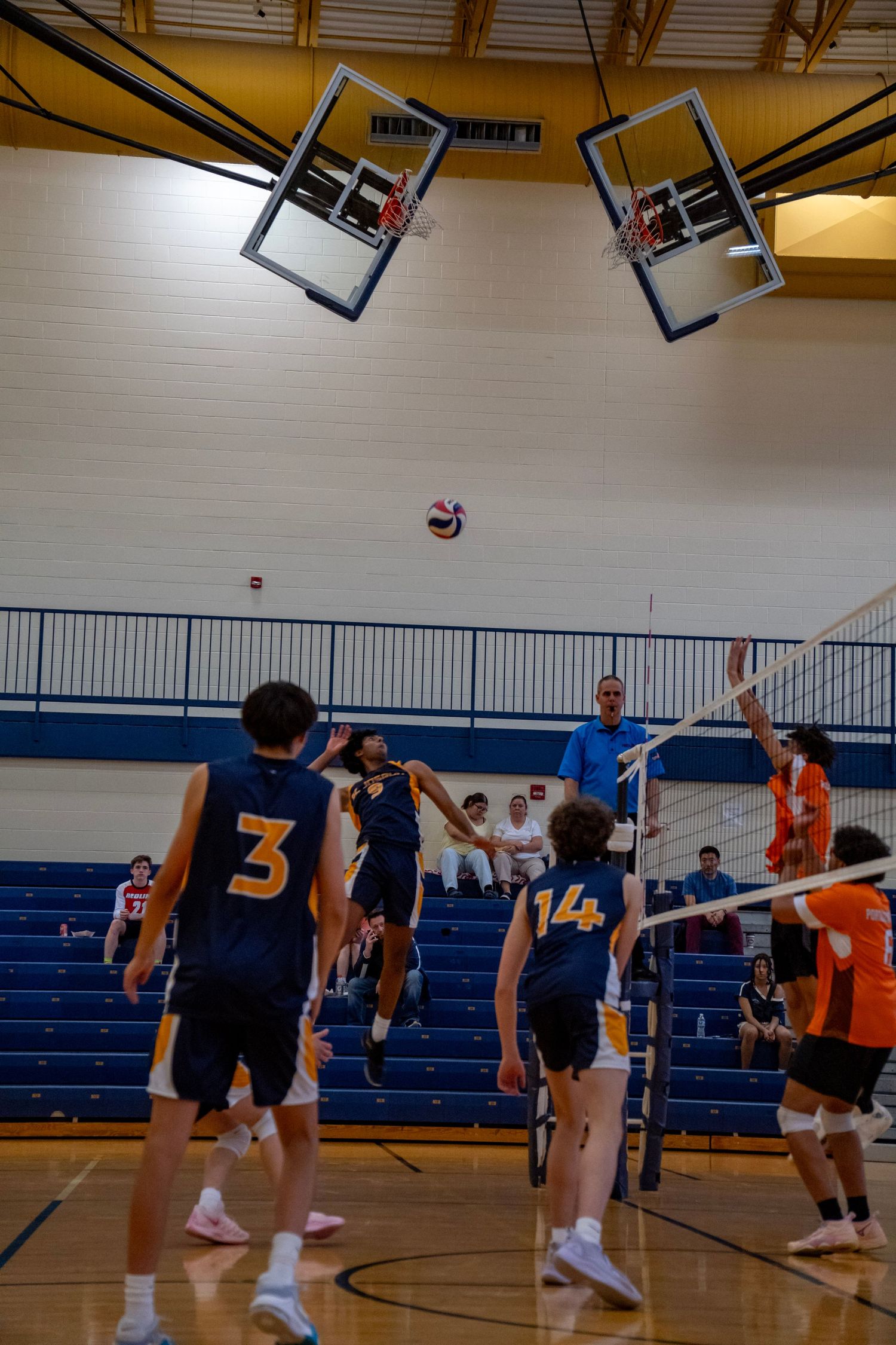 Volleyball match in progress with players at net in school gymnasium.