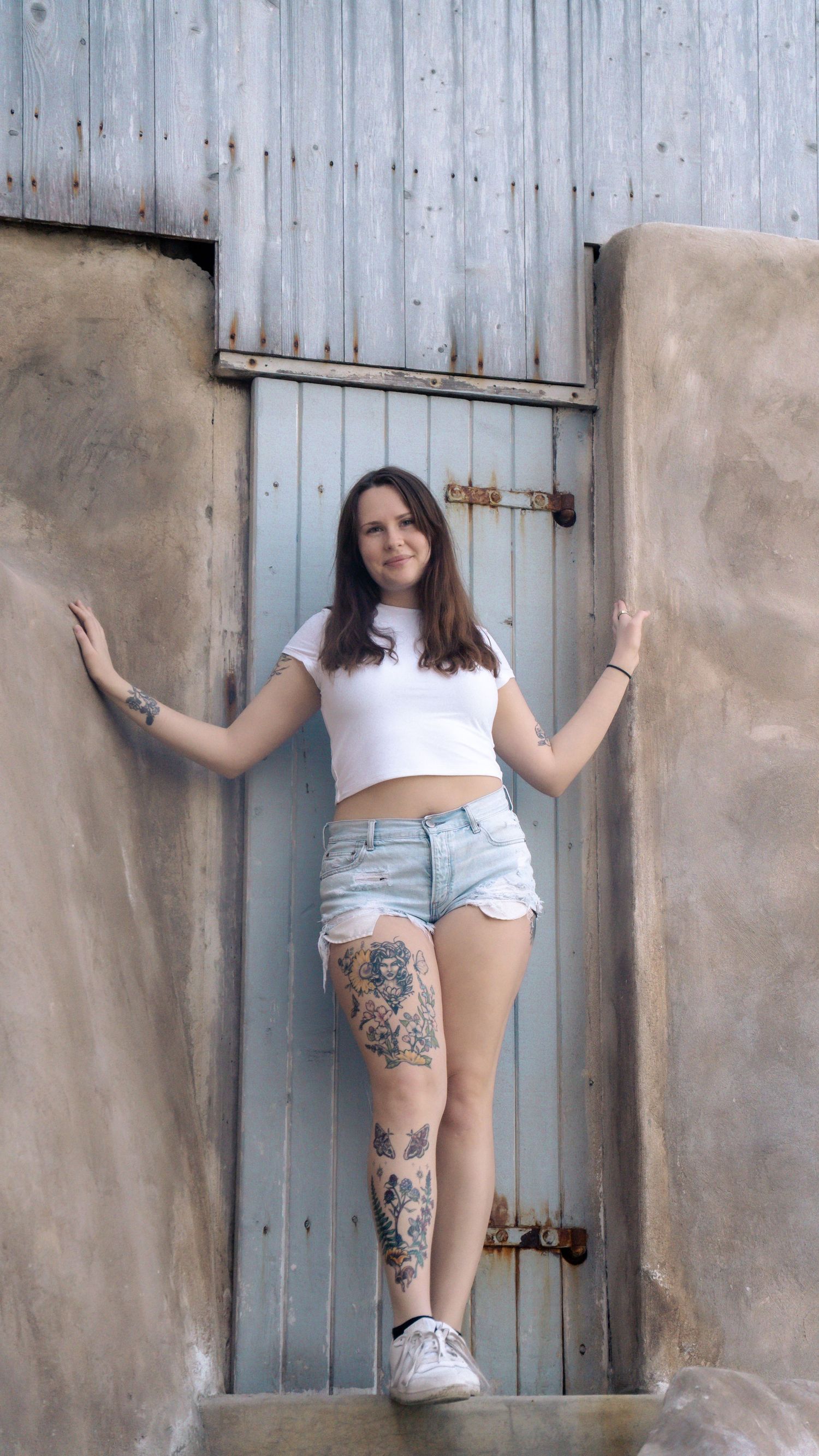 Summer fashion portrait against industrial backdrop with detailed leg tattoos.