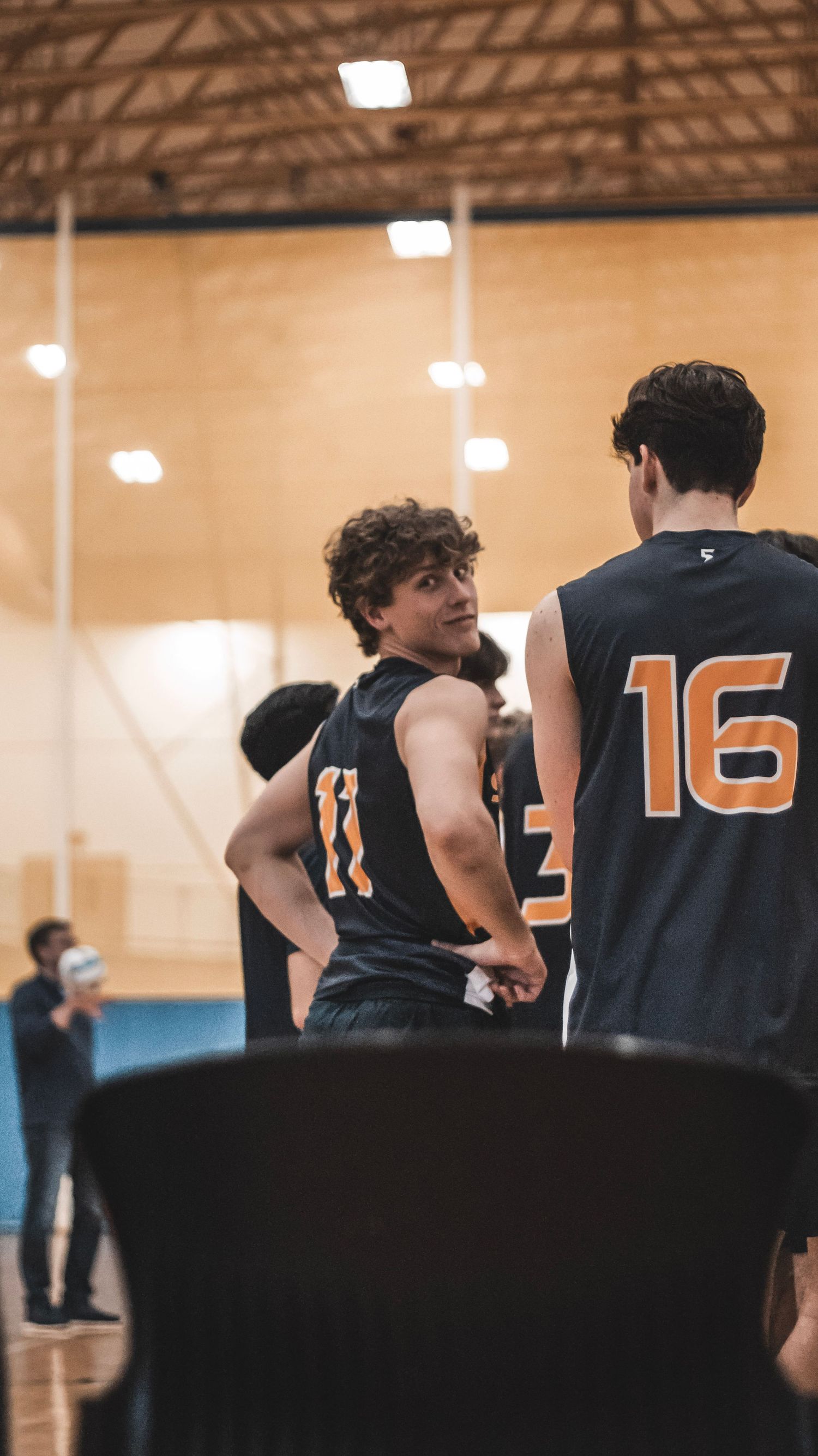 Players in black jerseys with orange numbers stand on the volleyball court.