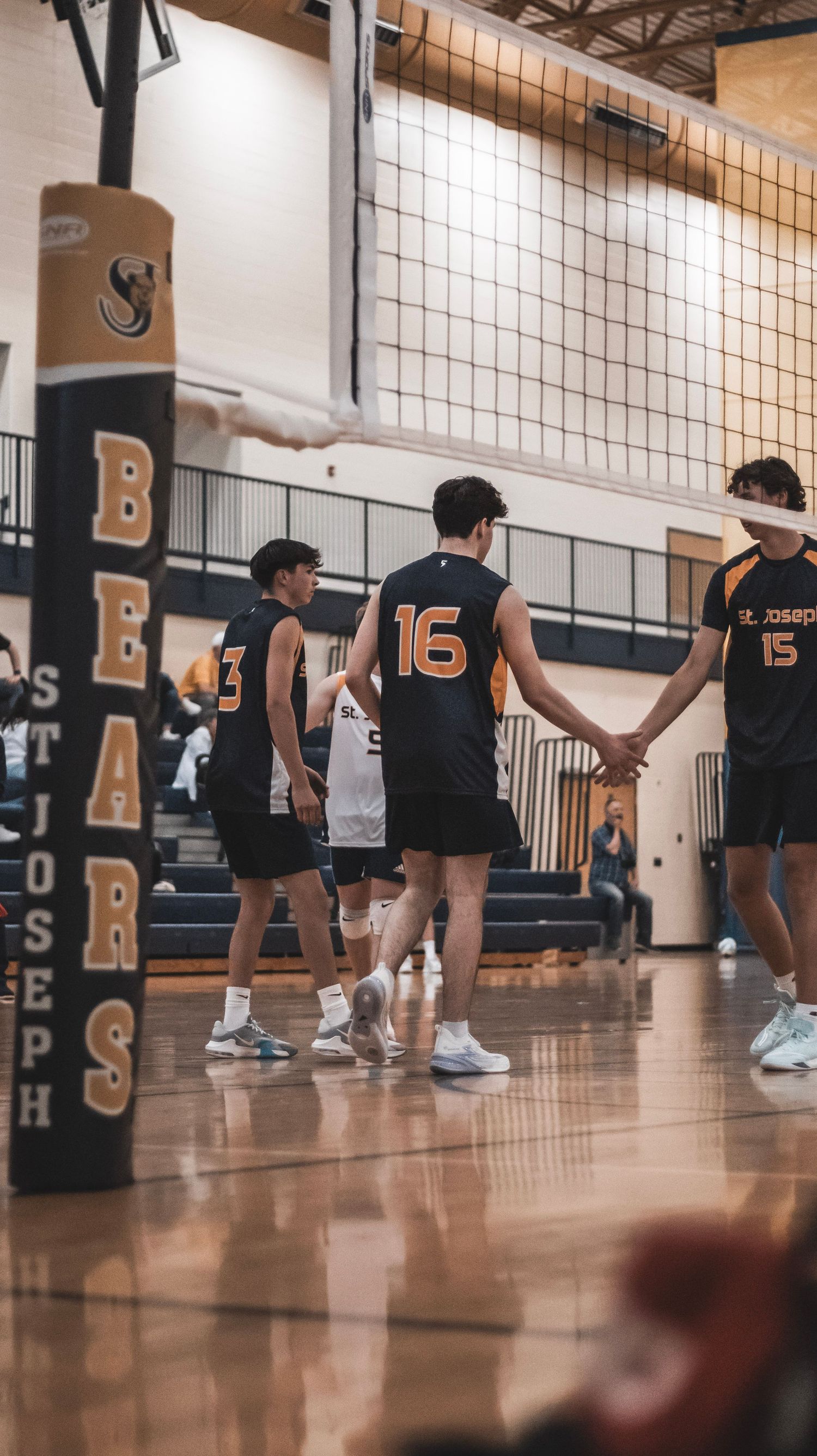 High school volleyball players in black jerseys stand together on a court during a game.