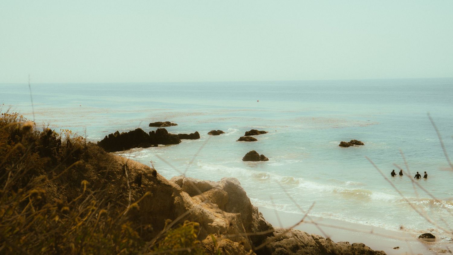 Rocky coastline with scattered boulders emerges from the misty ocean waters.