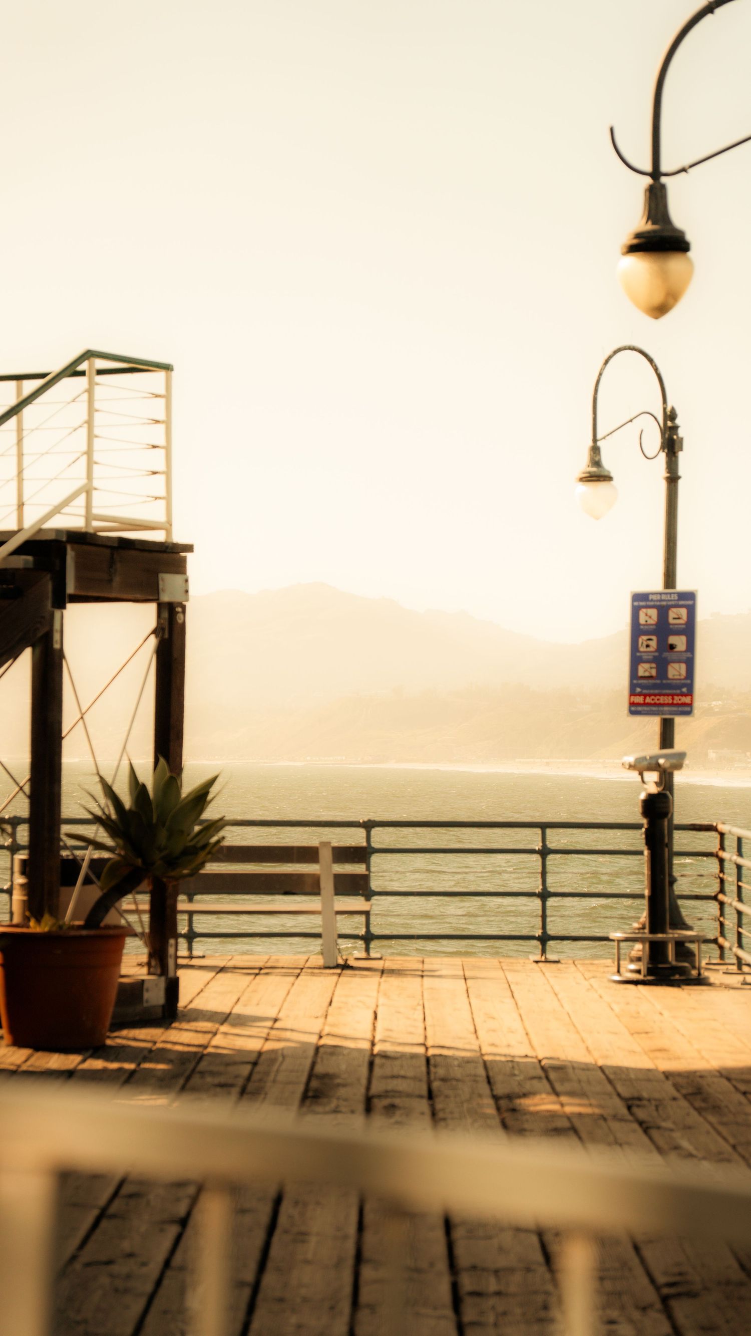 Sepia-toned view of pier boardwalk with vintage lamp post and ocean vista.