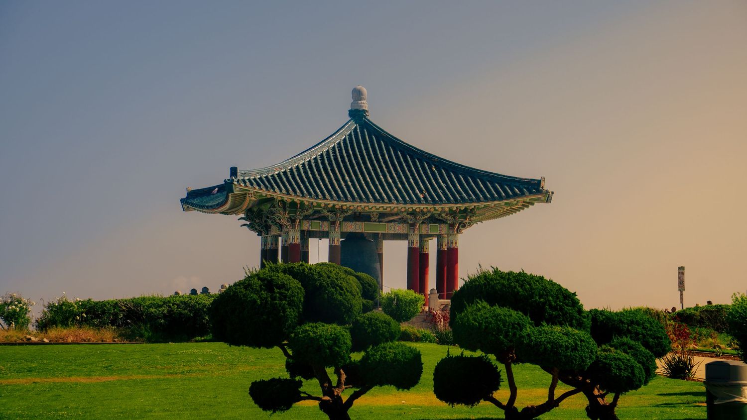 Low-angle view of Korean temple buildings with distinctive green roofs against a warm sunset sky.