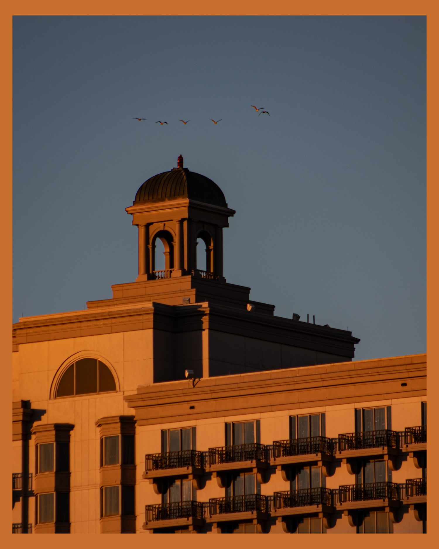 Sunset view of building dome with birds flying overhead against dusky sky.