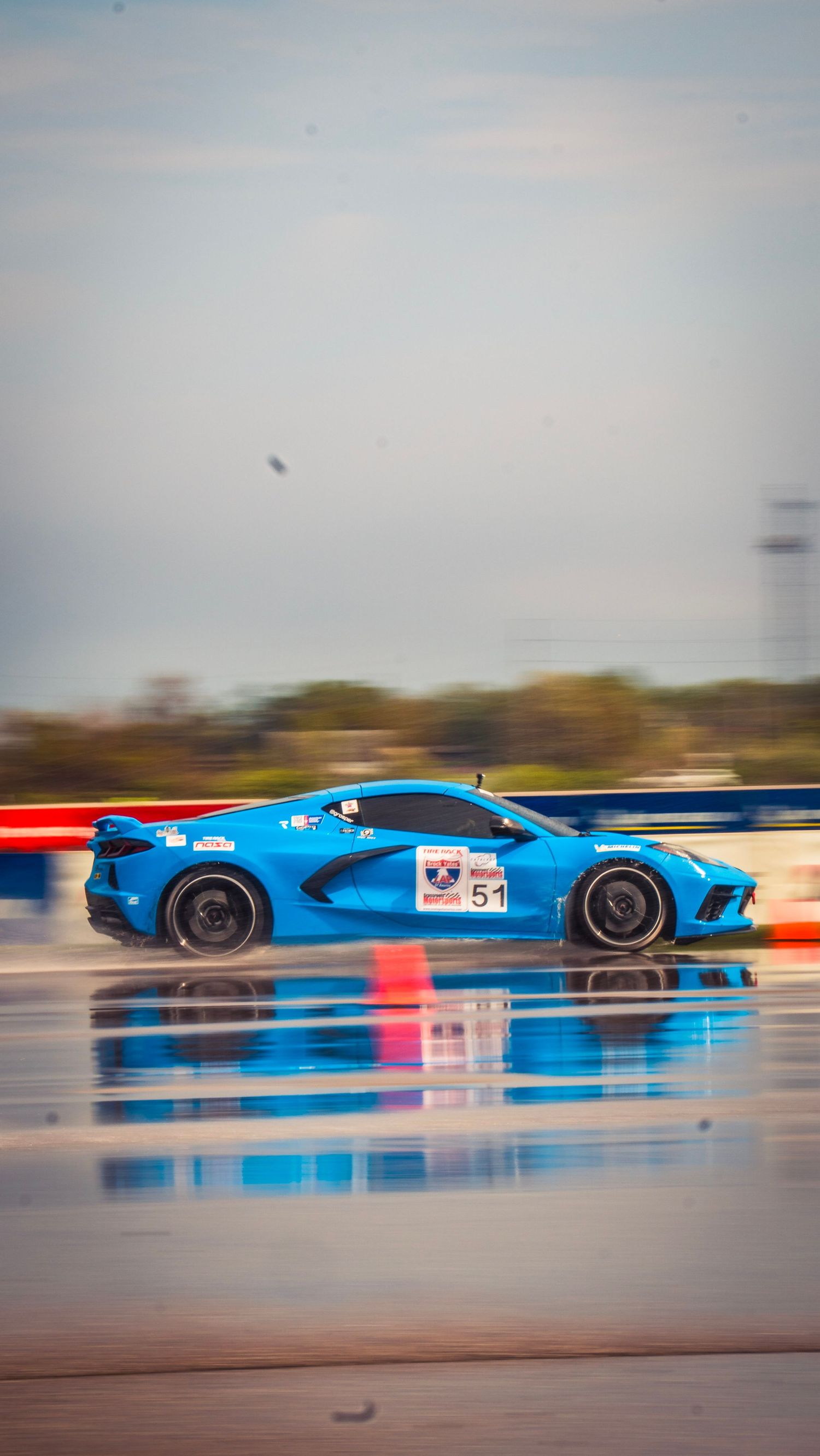 Bright blue sports car racing on a wet track with motion blur effect.