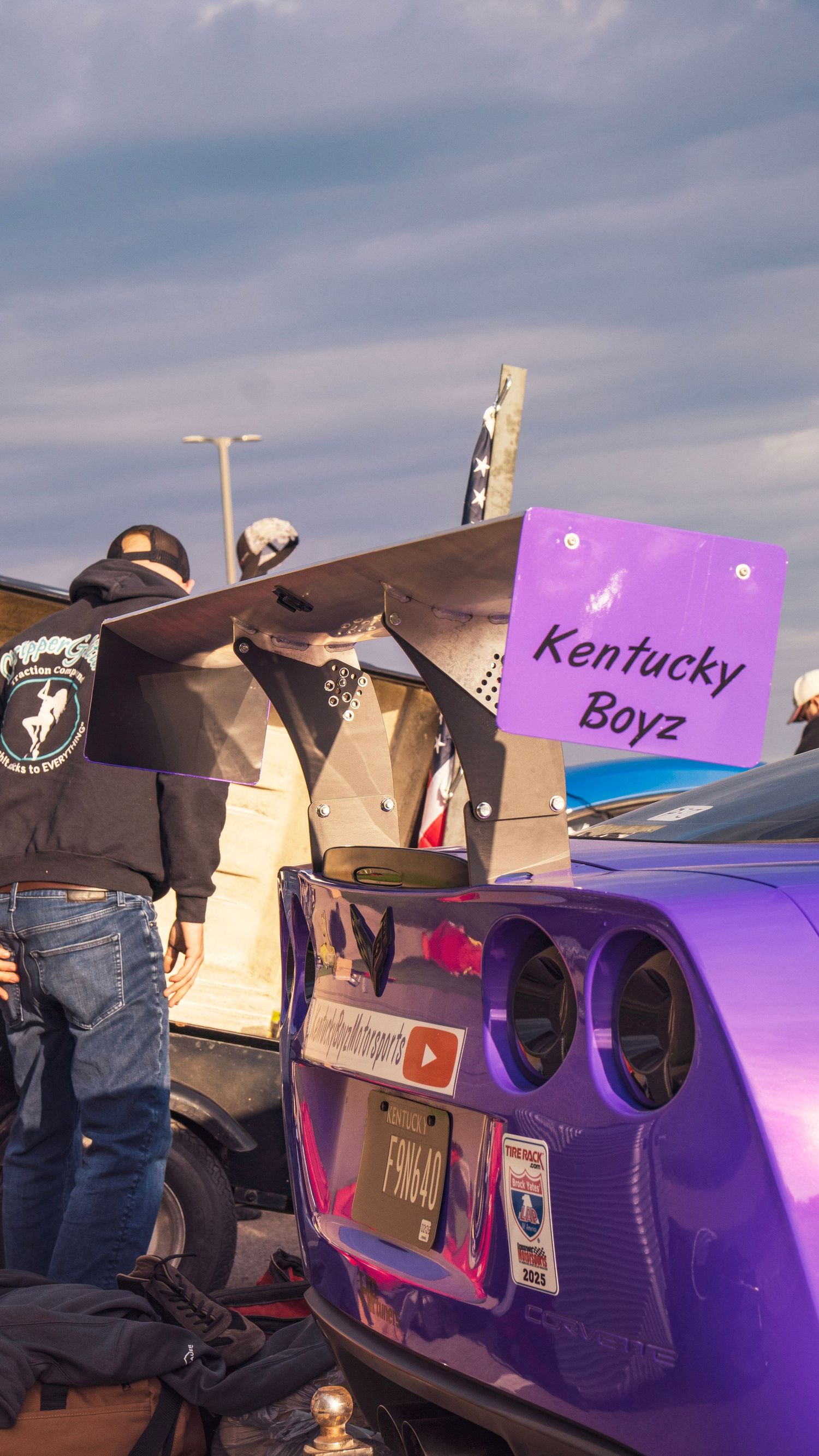 Purple Corvette with Kentucky Boyz sign displayed at a car meet during sunset.