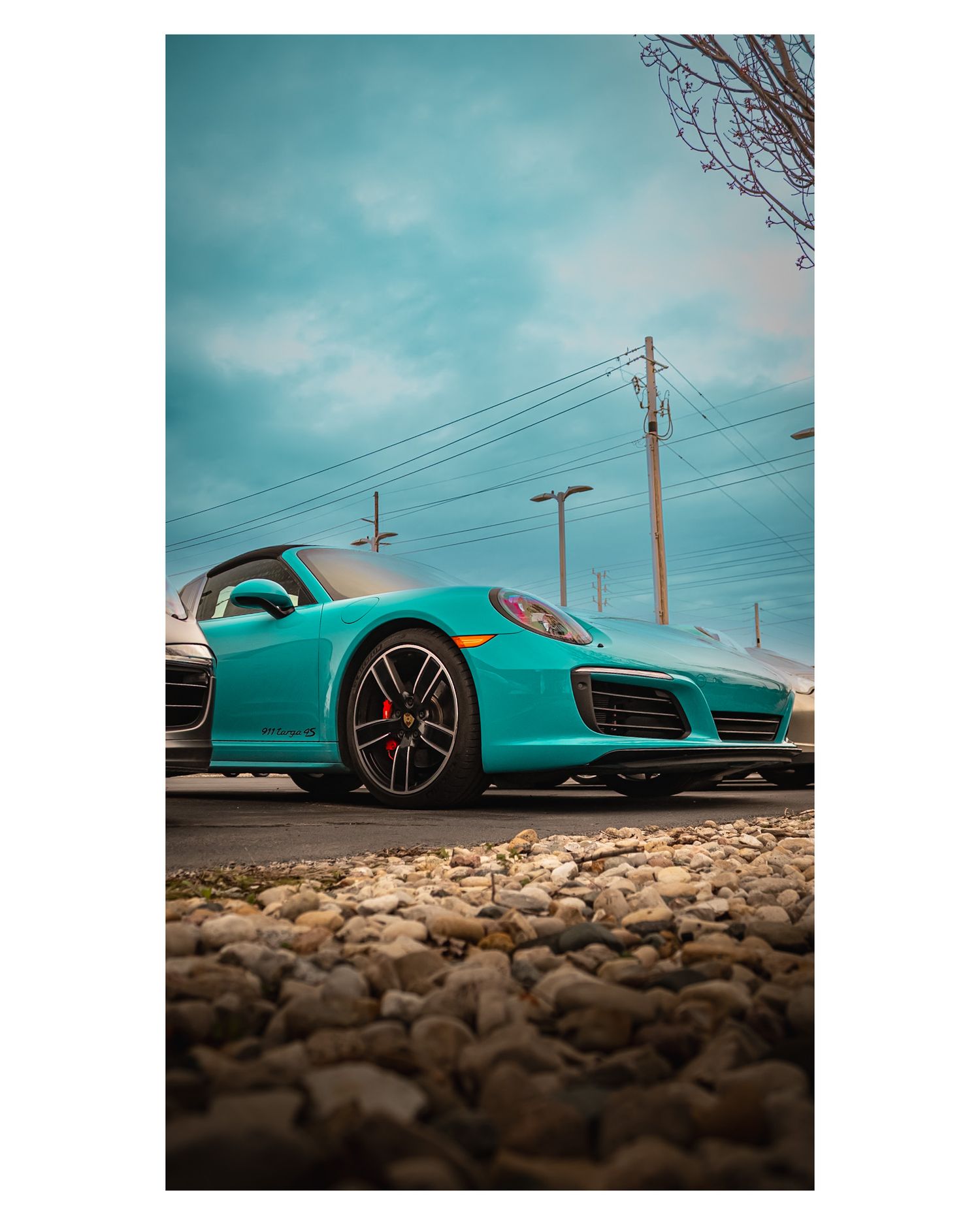 Low angle shot of a mint green Porsche 911 on gravel with utility poles in background.