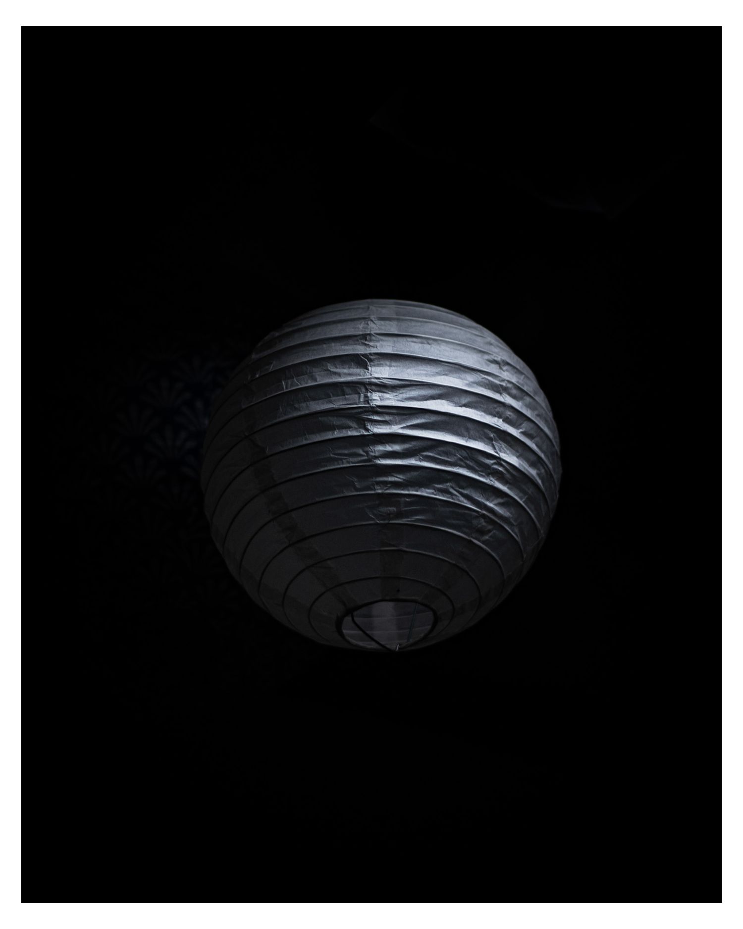 Black and white paper lantern glowing dramatically against dark background.