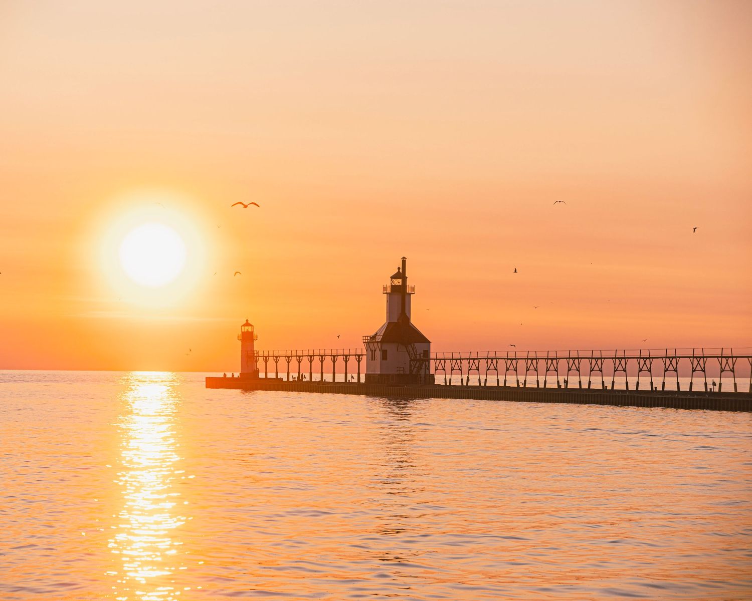 Lake Michigan lighthouse and catwalk silhouetted against warm orange sunset sky.