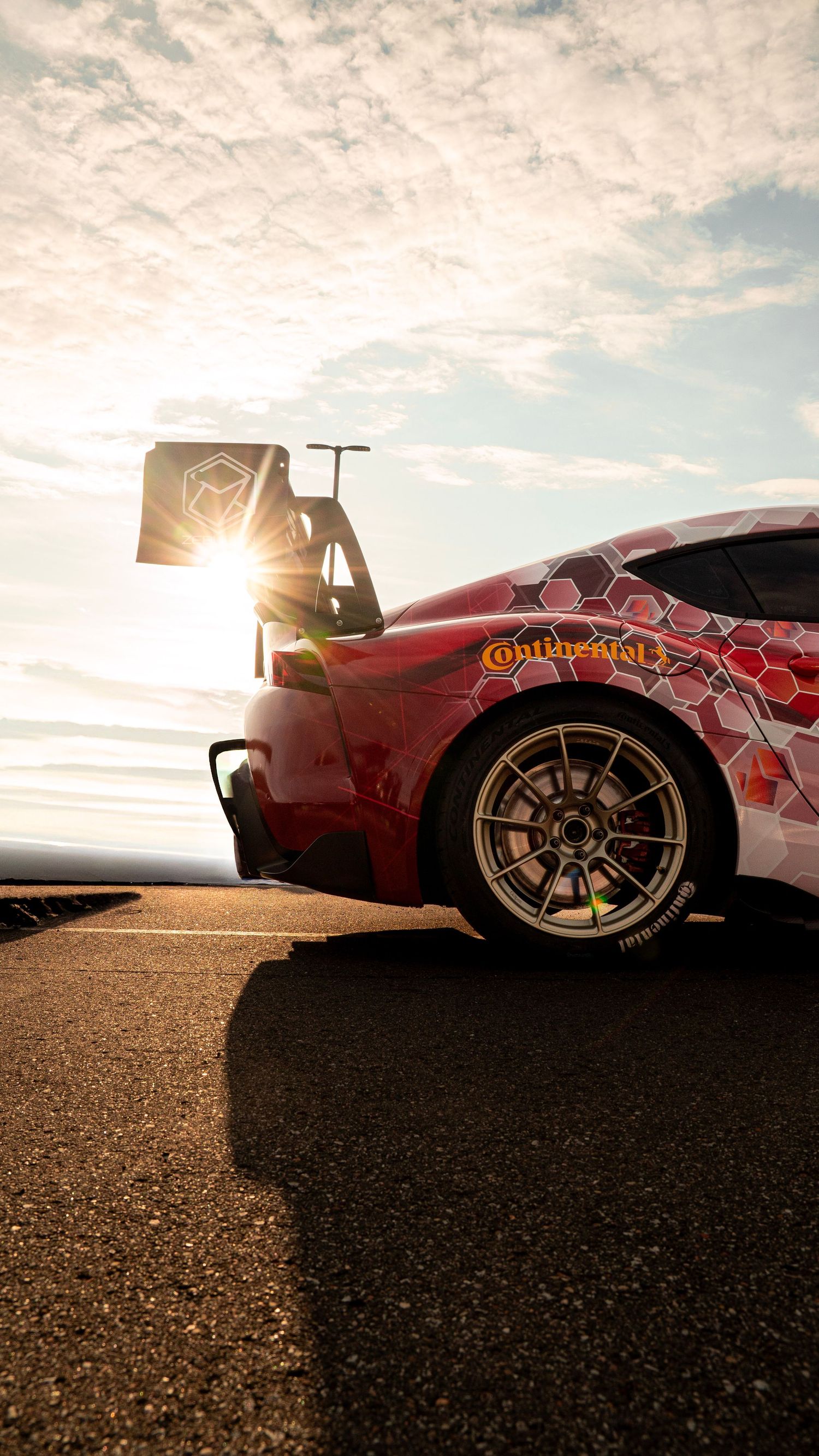 Dramatic sunset silhouette of race car with side-mounted exhaust and racing wing.