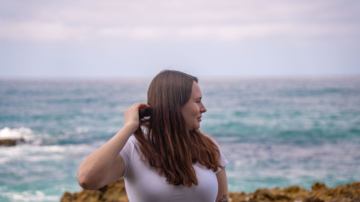 Side profile portrait with waves crashing against rocky coastline in background.