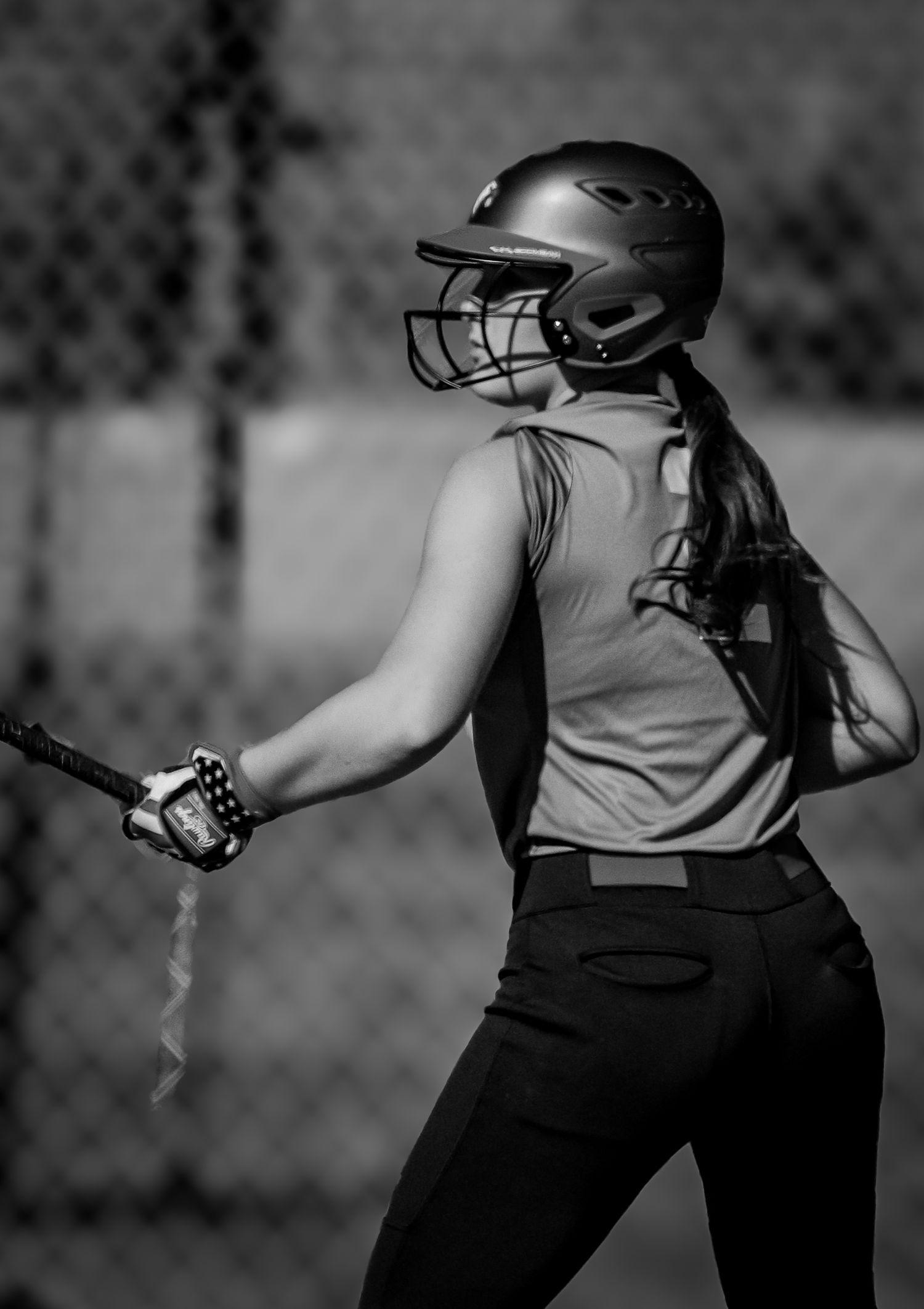 Black and white photo of a softball player in a batting stance wearing a helmet and sleeveless jersey.